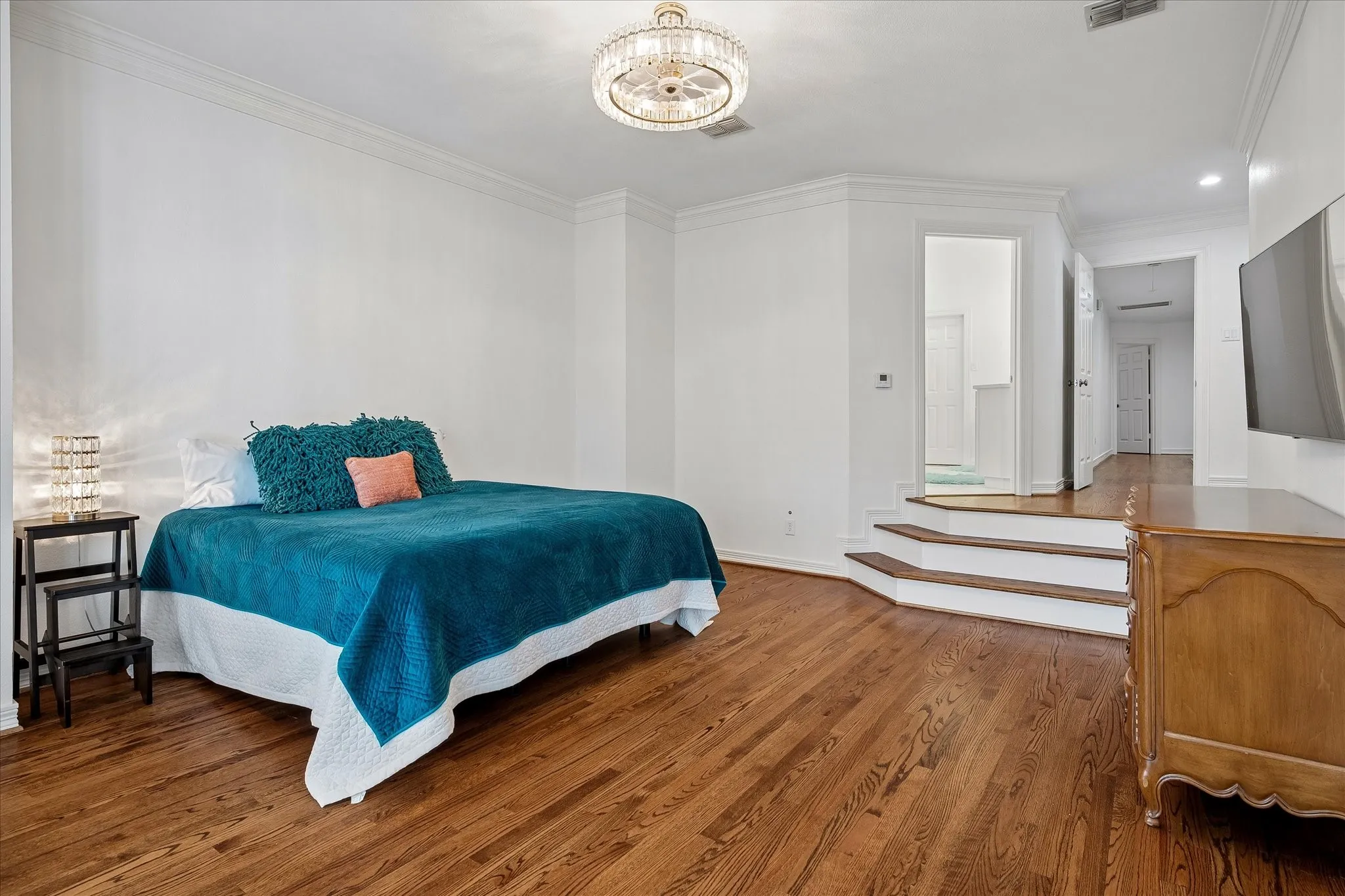 Hardwood flooring, crown molding, tiered steps, a built-in ceiling light fixture, and a wall-mounted television