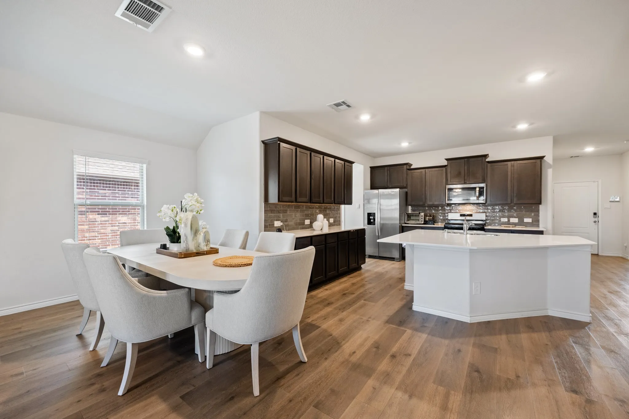 Open-concept layout featuring wood-finish flooring, dark wood cabinetry, a white kitchen island, and recessed lighting