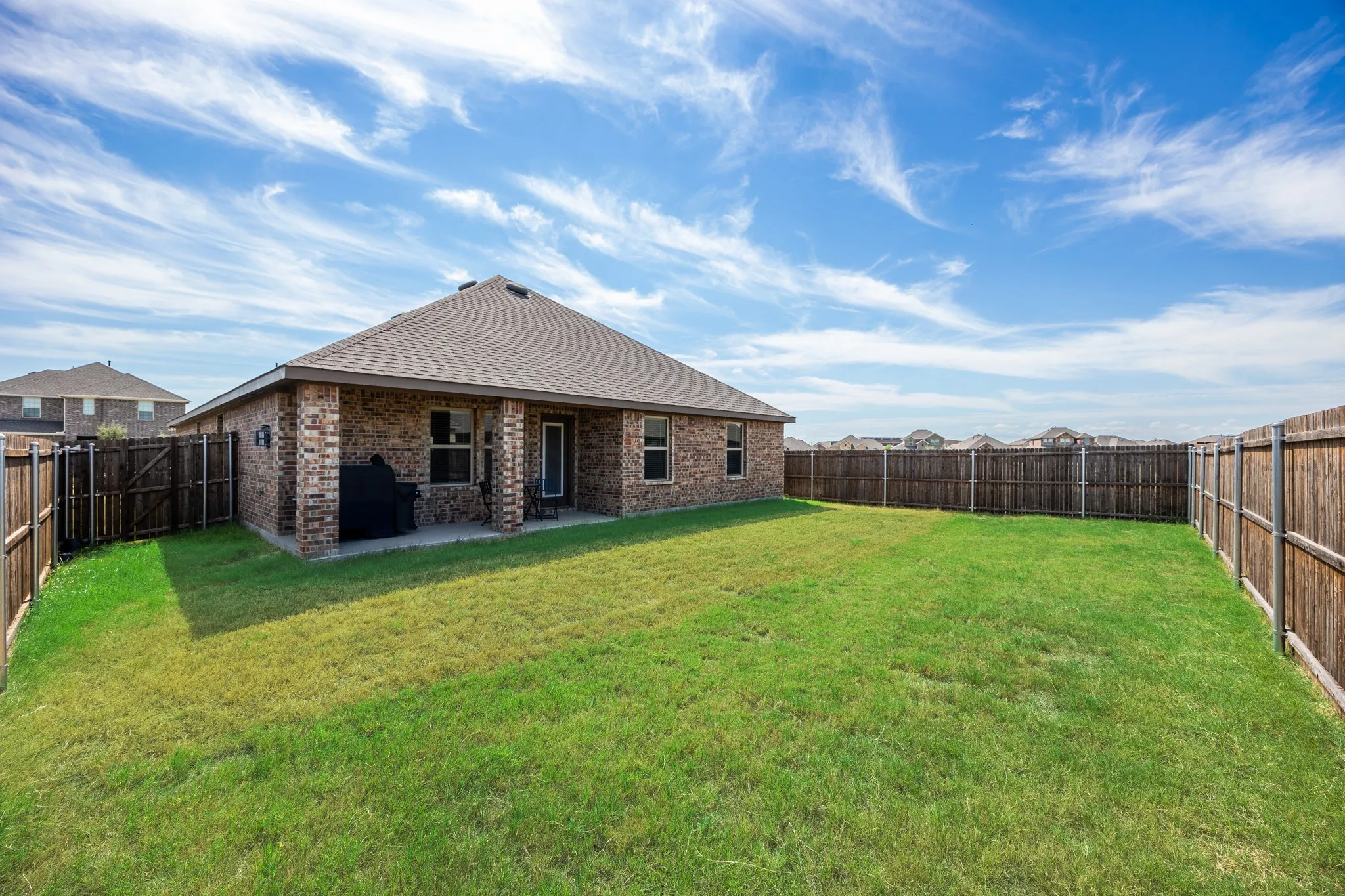 Expansive backyard featuring a manicured lawn, full privacy fencing, and a covered patio with brick columns