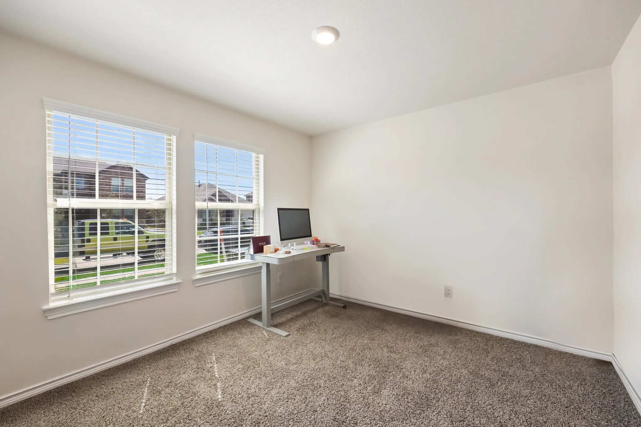 Two double-hung windows with blinds, recessed ceiling light, and neutral carpet