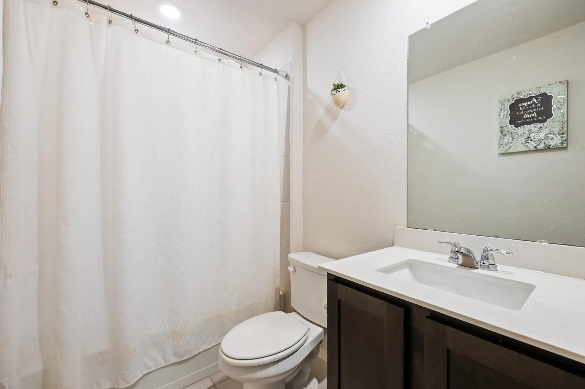 Vanity with a white countertop and dark wood-finish cabinetry, chrome fixtures, and a frameless mirror