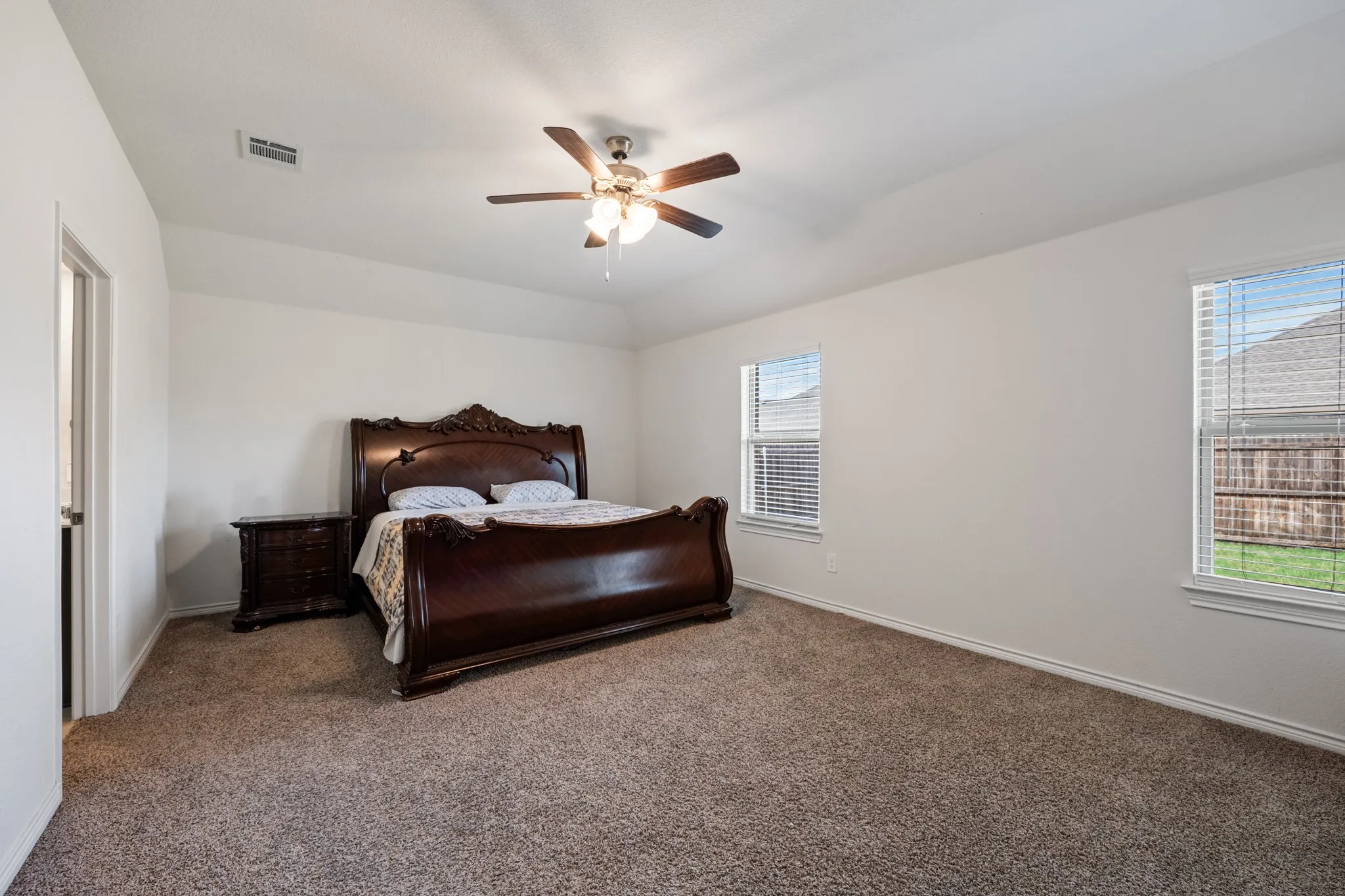 Vaulted ceiling with a ceiling fan, two windows with blinds, and neutral carpeting