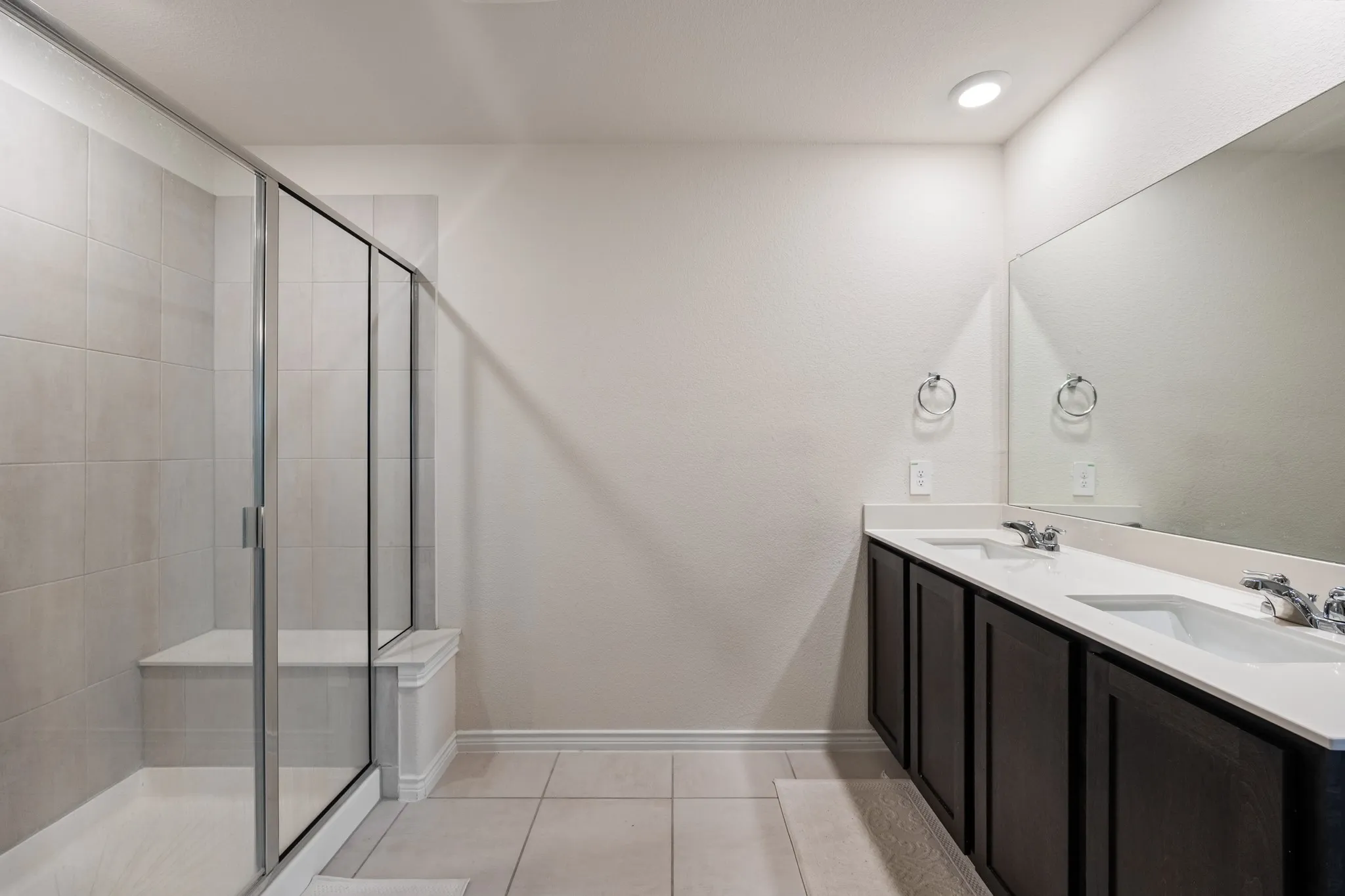 Dual vanity with integrated sinks, full wall mirror, recessed lighting, and a walk-in shower with a built-in bench