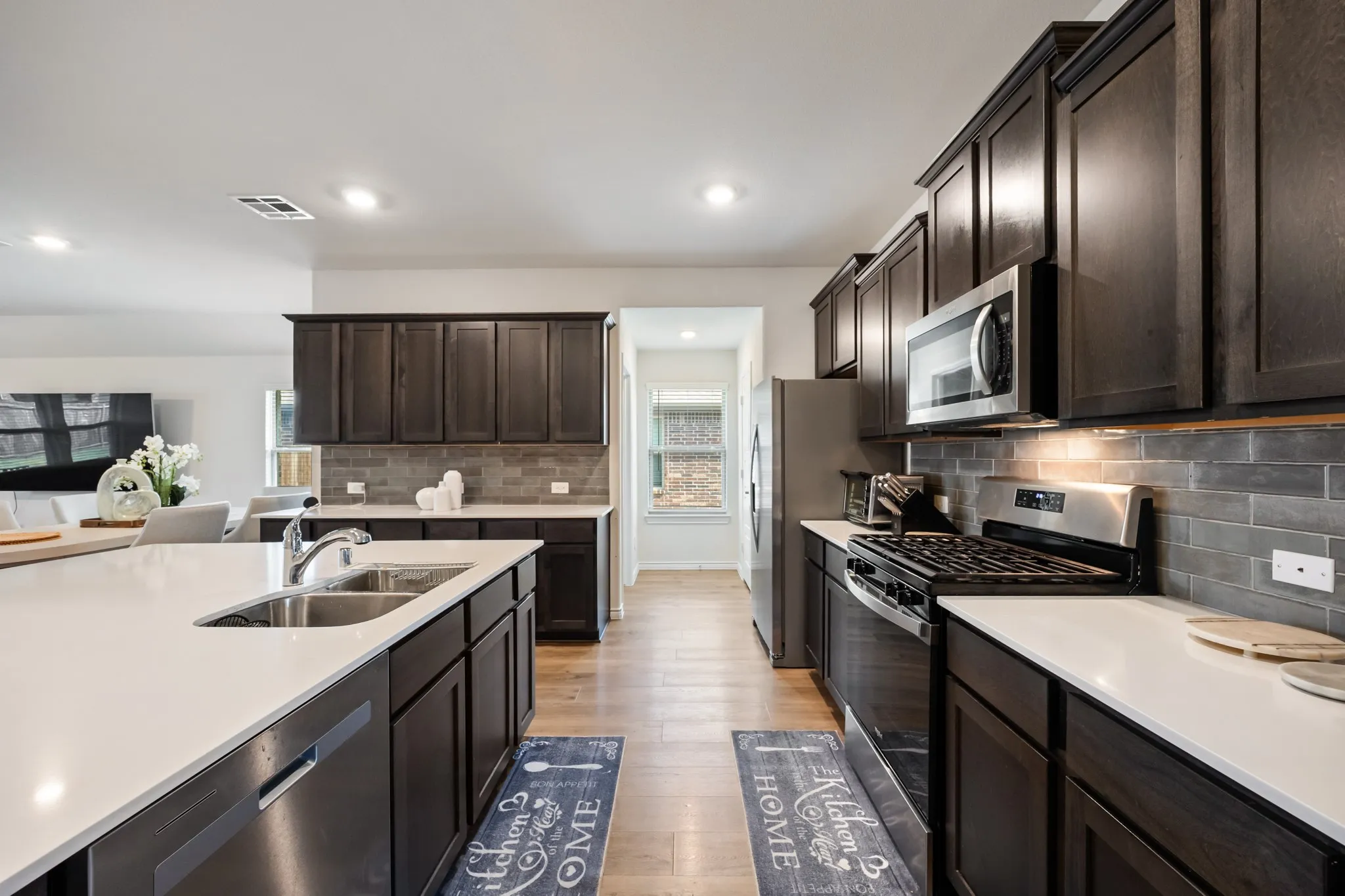 Spacious kitchen featuring dark wood cabinetry, stainless steel appliances, a large island with an undermount sink, white countertops, and wood-finish flooring
