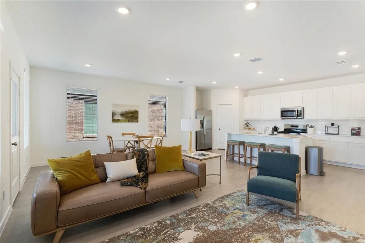 Open-concept living space featuring wood-finish flooring, recessed lighting, and a kitchen with white cabinetry, stainless steel appliances, and a central island with seating