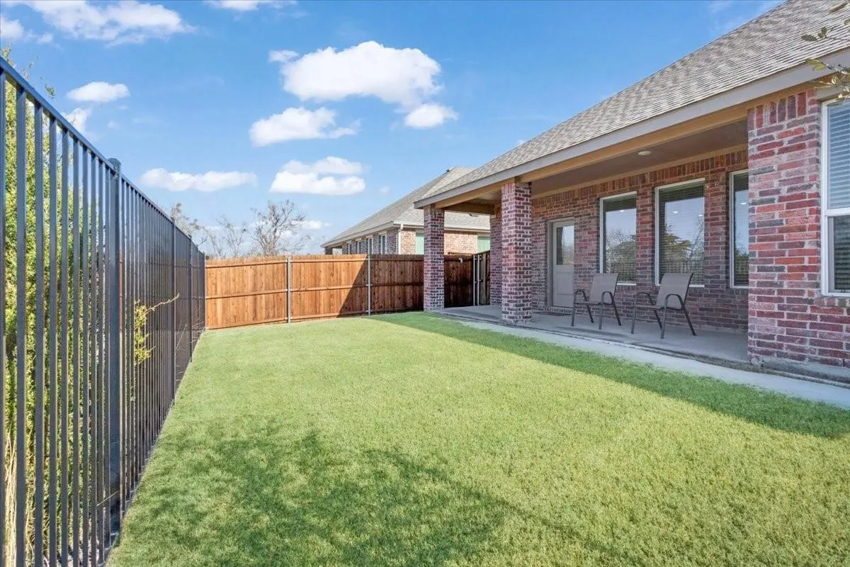 Expansive backyard featuring a manicured lawn, a covered patio, and a combination of black metal and privacy fencing