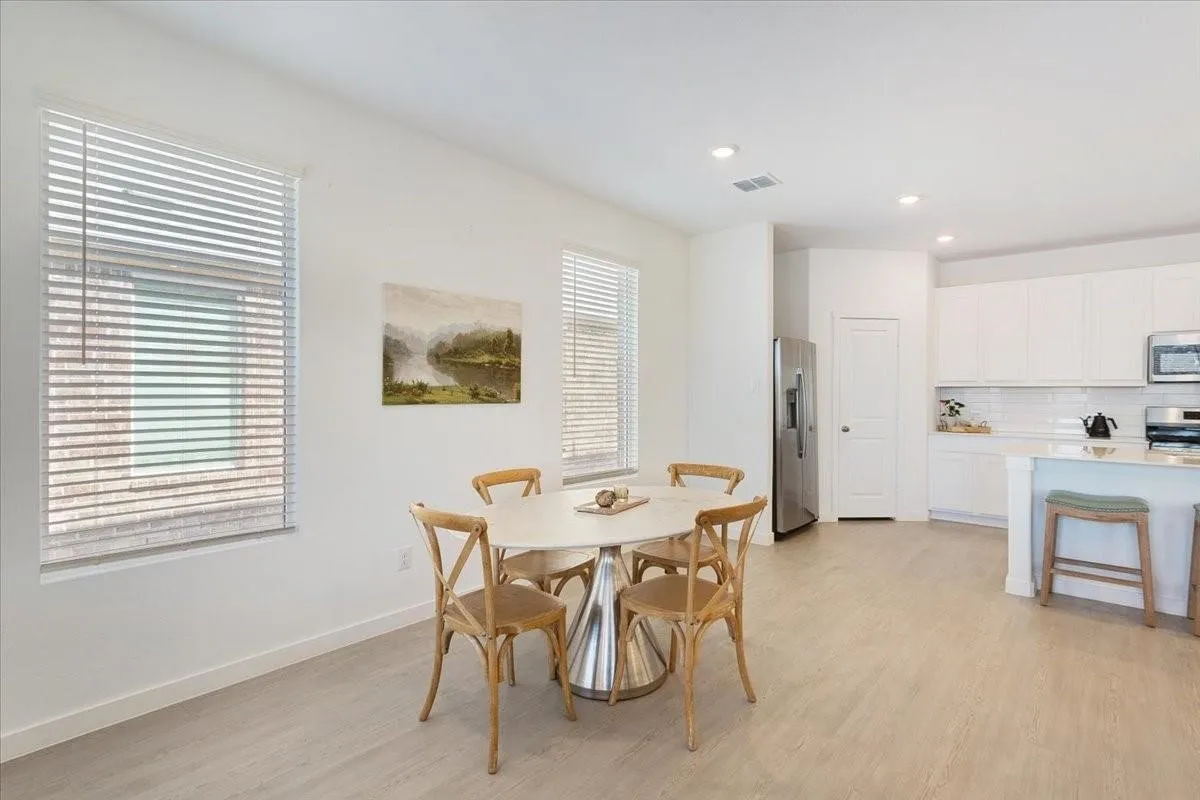 Open-concept kitchen and dining area featuring light wood-finish flooring, white cabinetry, stainless steel appliances, and recessed lighting