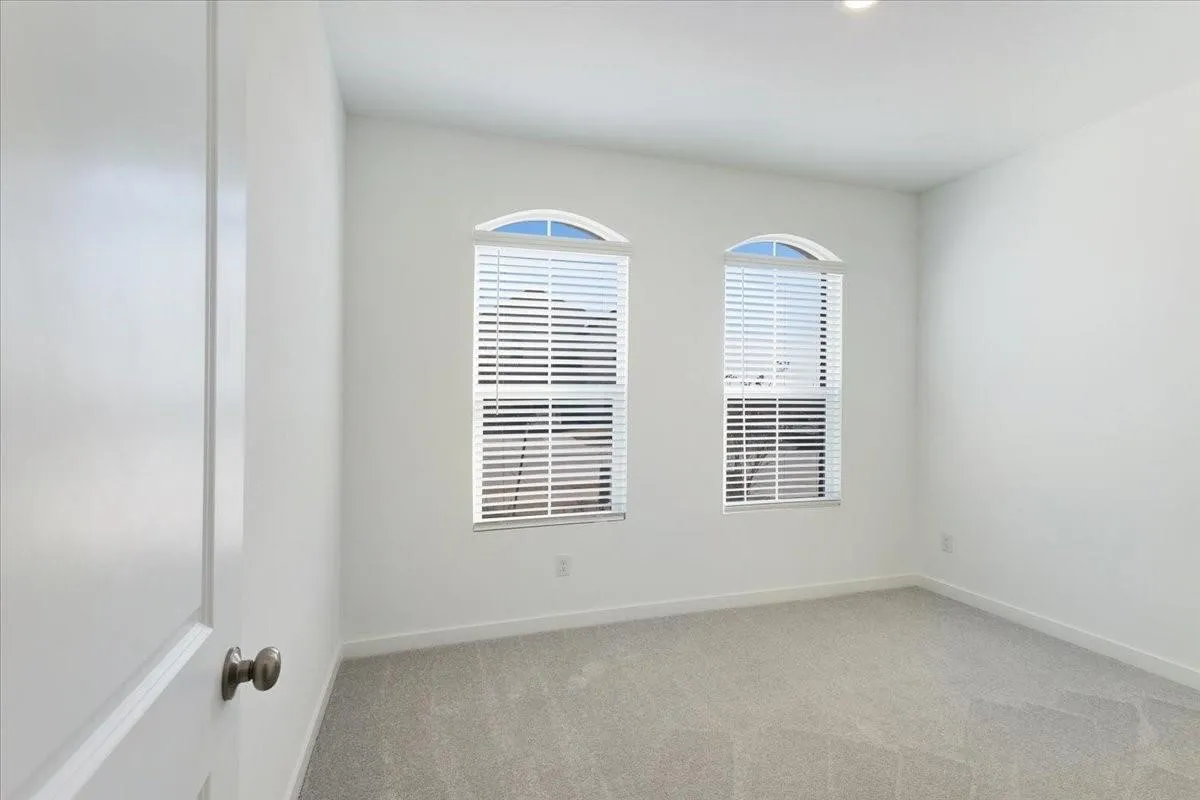 Arched windows with blinds, recessed lighting, and light-toned carpet flooring