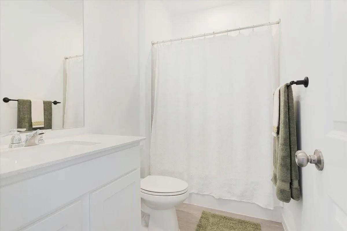 White vanity with an integrated sink and clear faucet, large wall mirror, and a white shower curtain with a metal rod