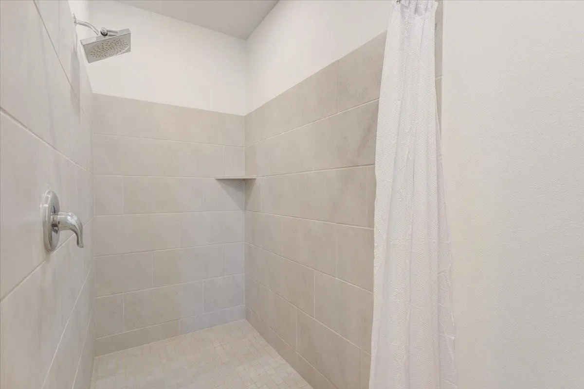 Tiled shower surround with a built-in corner shelf, chrome showerhead, and coordinating chrome faucet