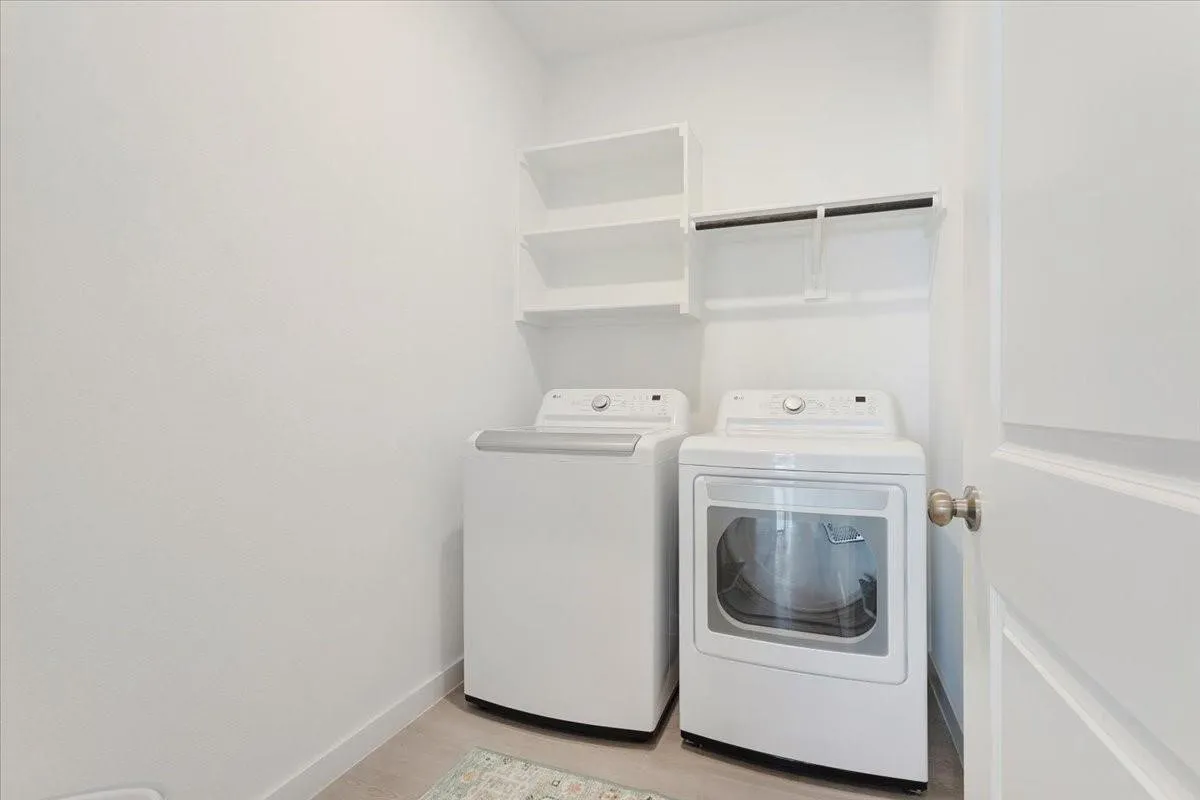 Integrated laundry area featuring built-in shelving, a clothes hanging rod, and light-toned flooring