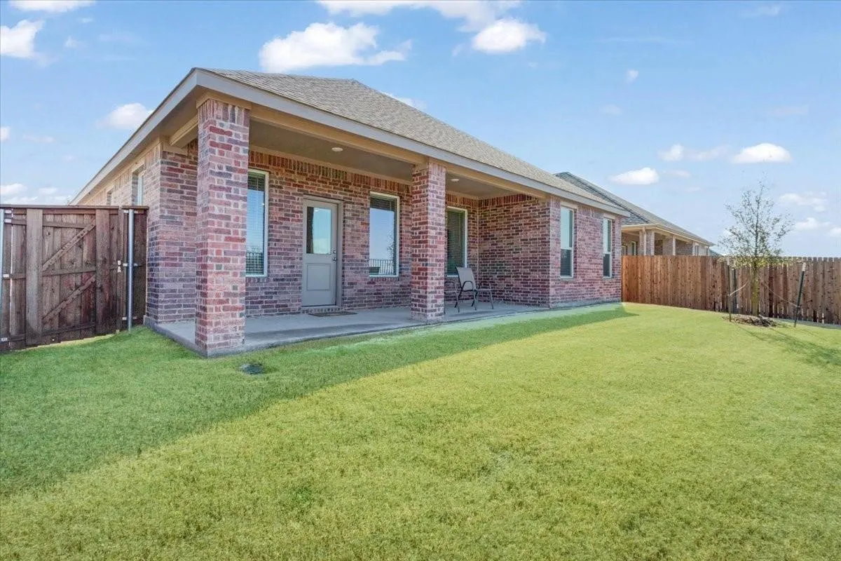 Expansive backyard featuring a covered patio, red brick exterior, multiple windows, and a wood privacy fence