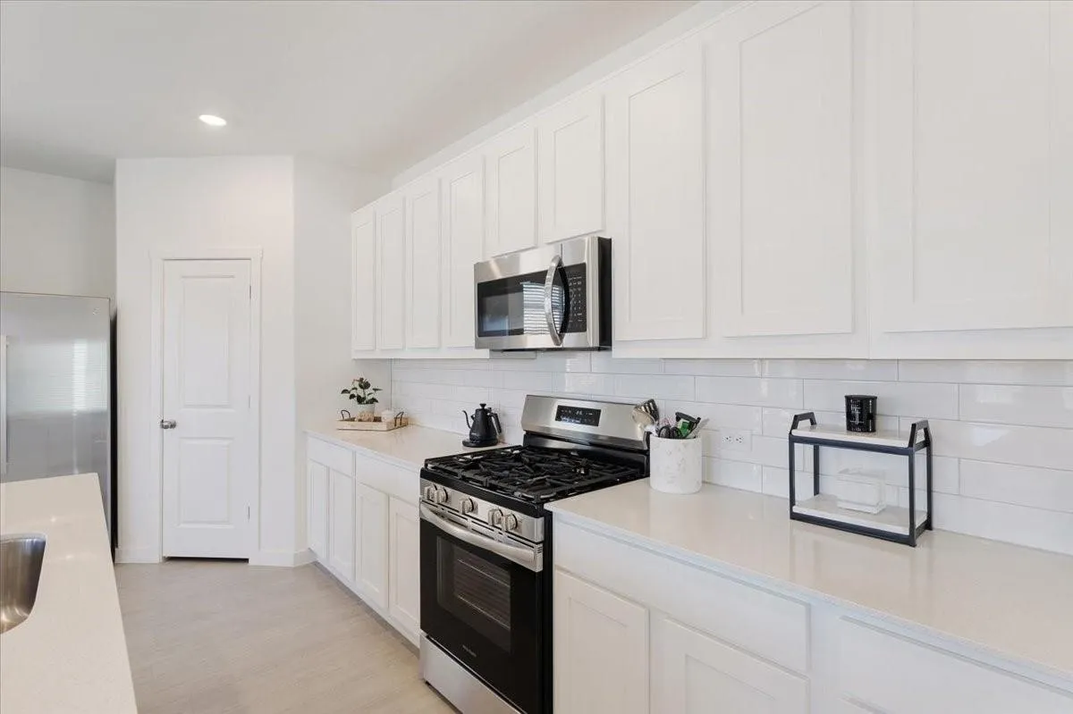 Contemporary kitchen with white shaker-style cabinetry, stainless steel appliances, light-toned countertops, and subway tile backsplash