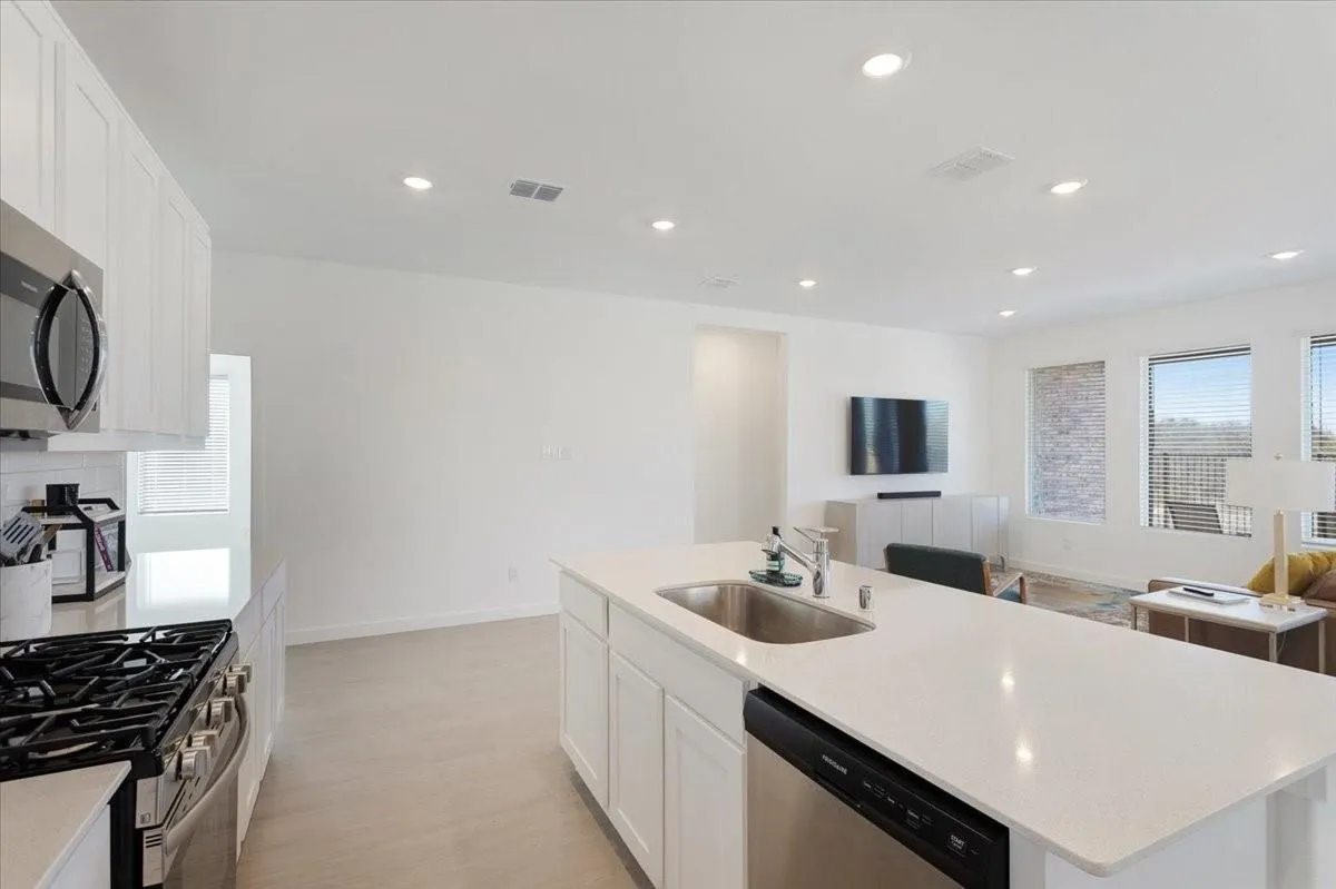 Open-concept living space featuring a kitchen with white cabinetry, stainless steel appliances, a center island with an undermount sink, and recessed lighting