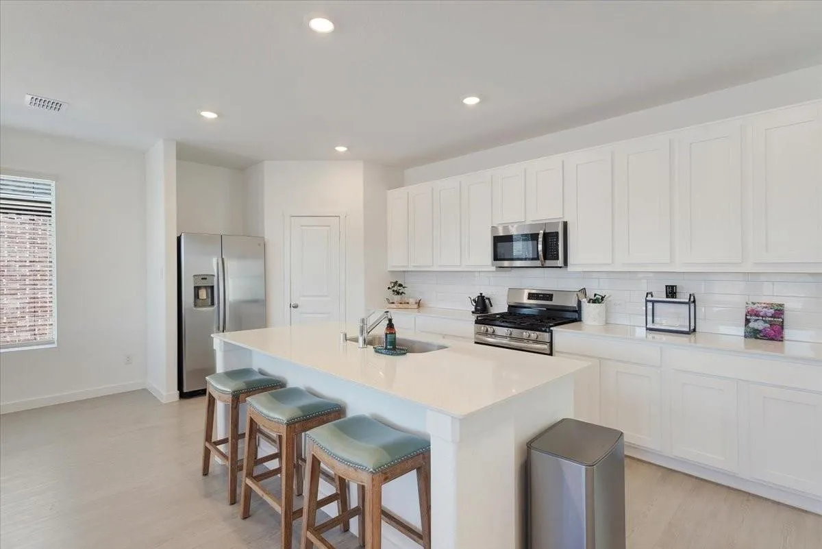 Contemporary kitchen featuring white shaker cabinetry, stainless steel appliances, a large center island with seating, recessed lighting, and light wood-finish flooring