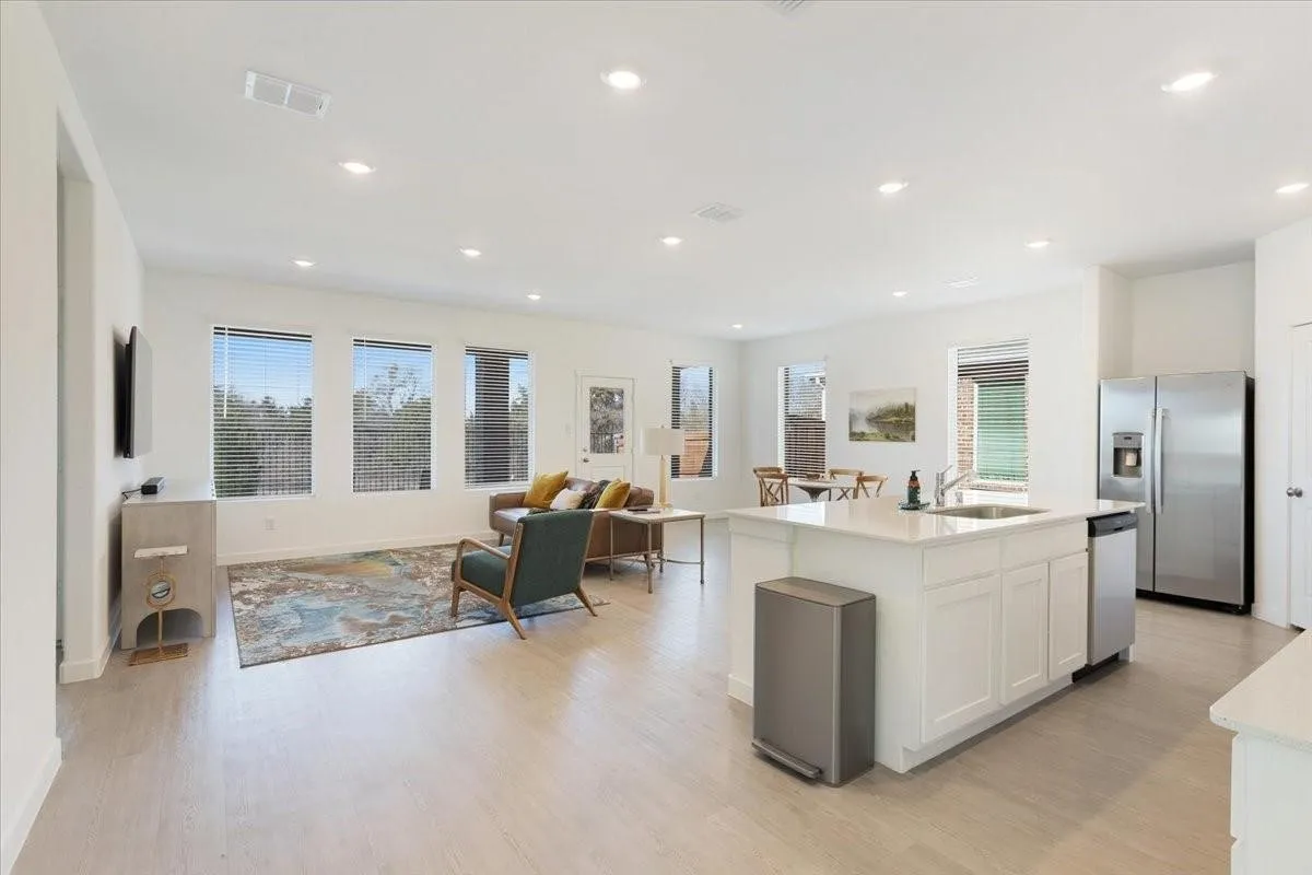 Open-concept living area featuring wood-finish flooring, recessed lighting, multiple windows, a kitchen island with a sink, and stainless steel appliances