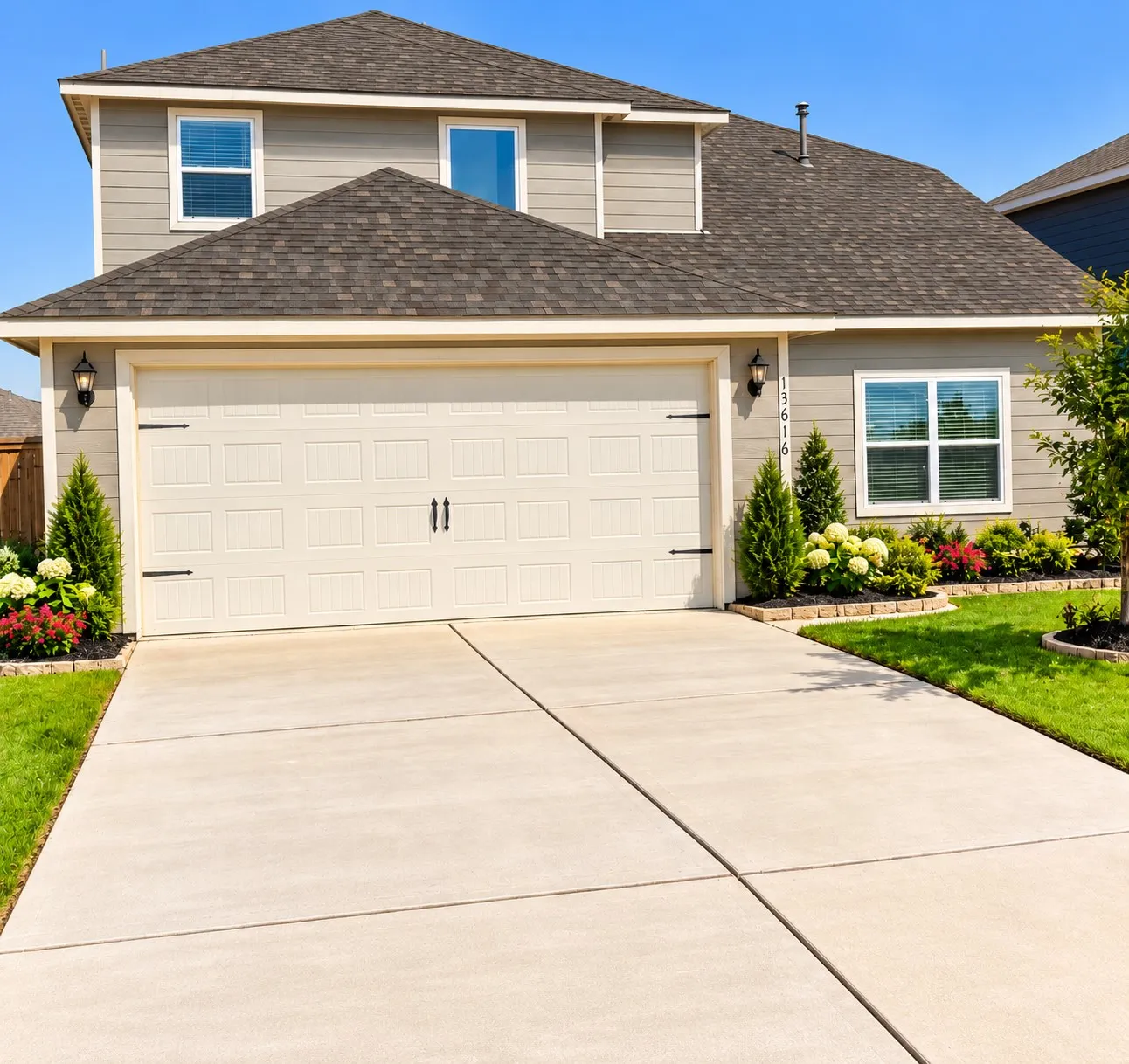 Two-story residential exterior featuring gray siding, a dark shingle roof, a two-car garage with decorative hardware, and a paved driveway