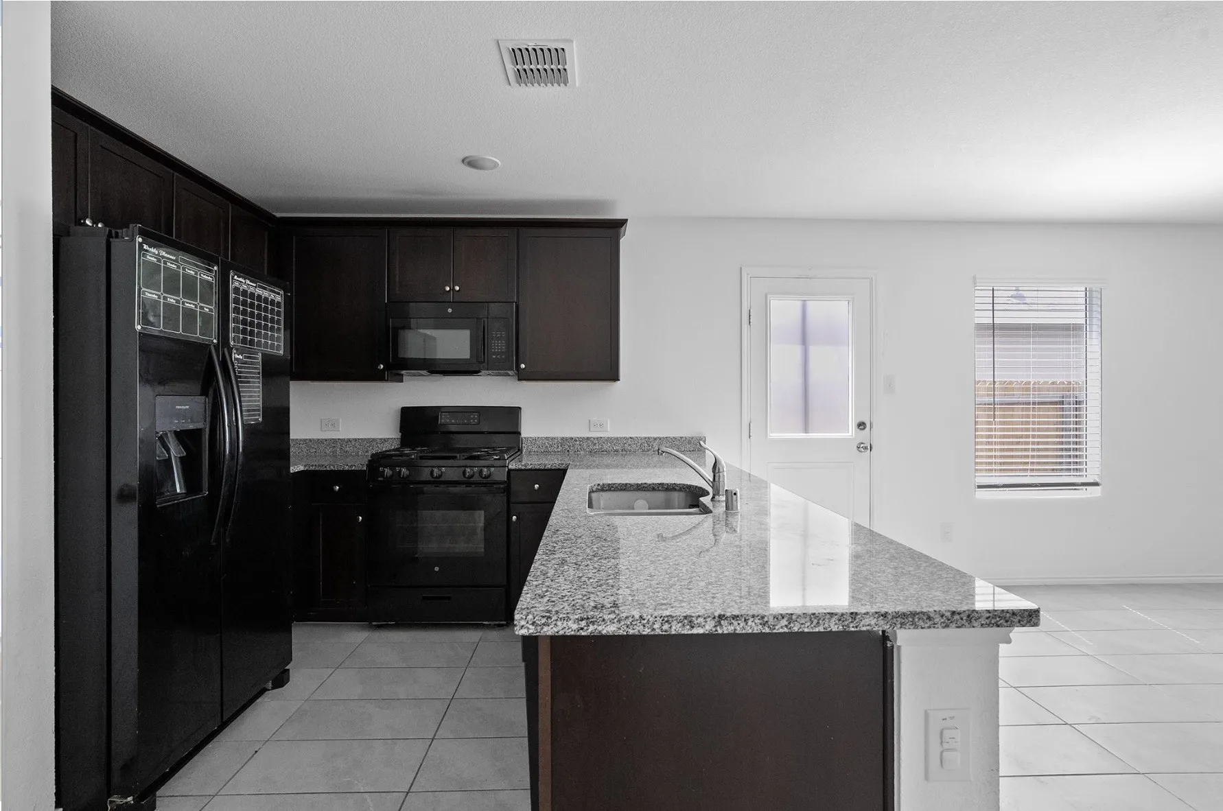 Kitchen featuring dark wood cabinetry, granite countertops, tile flooring, and integrated black appliances