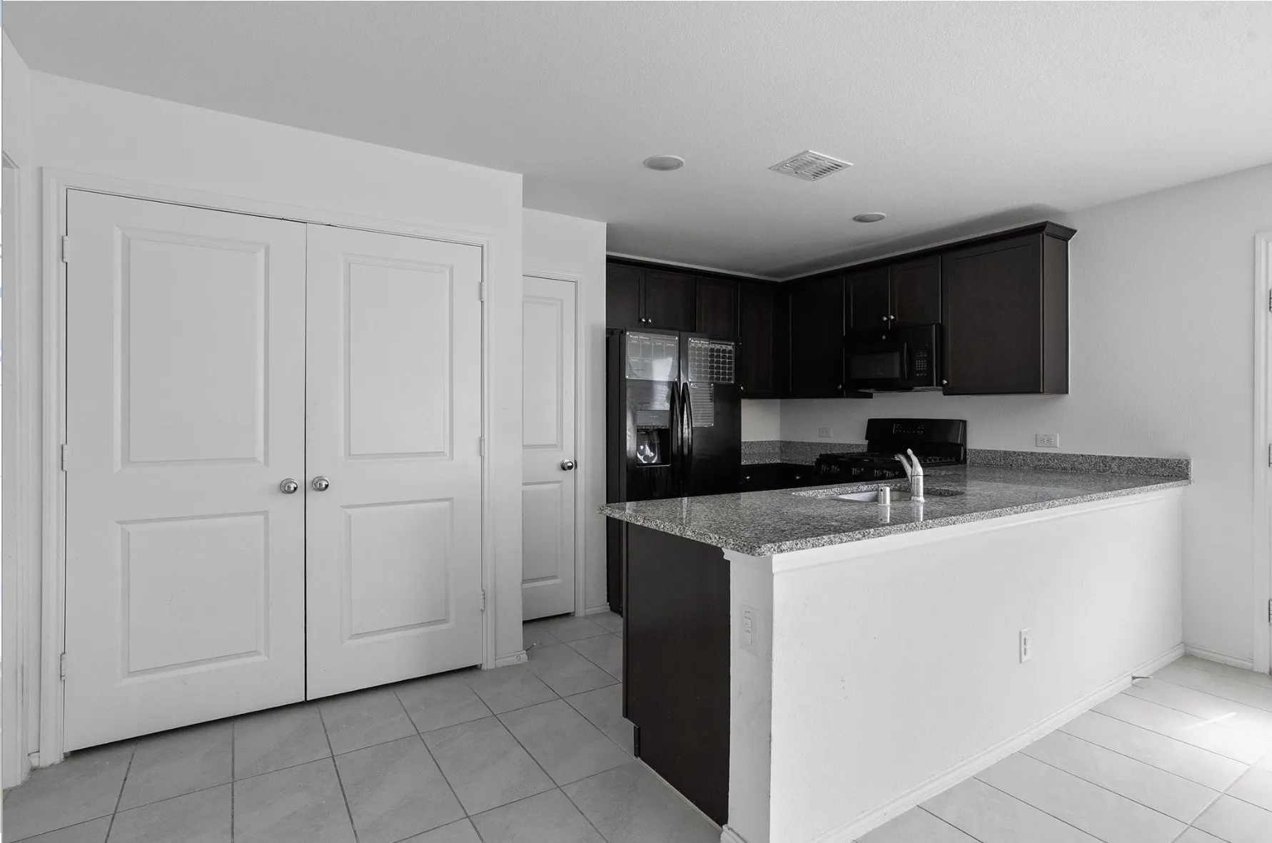 Dark wood-finish cabinetry, black appliances, granite-style countertops, and tile flooring