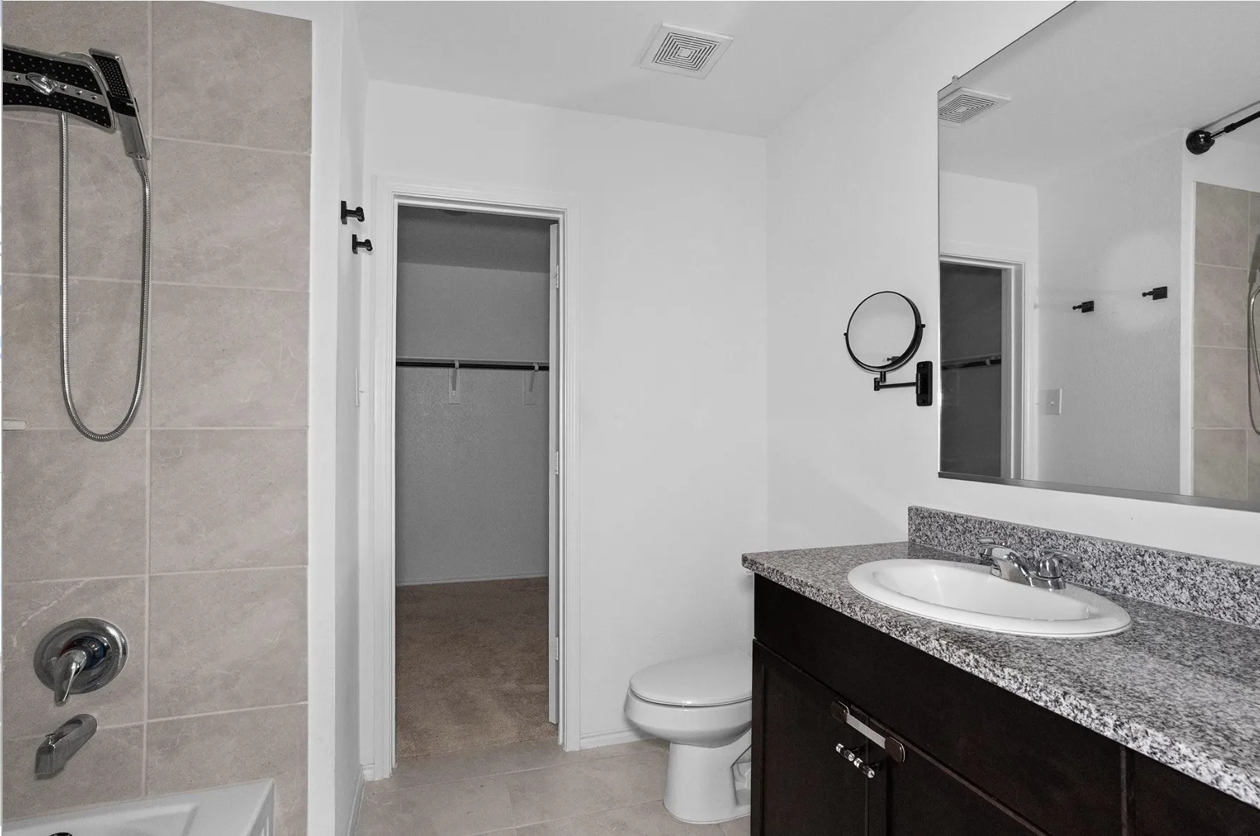 Bathroom featuring a shower with light-toned wall tile, a dark wood-finish vanity, an oval undermount sink, and a speckled countertop