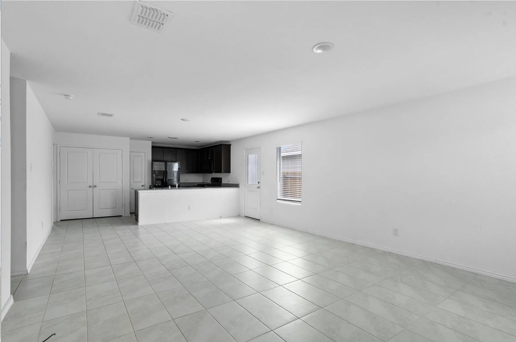 Spacious interior with neutral tile flooring, recessed lighting, and a kitchen featuring dark wood cabinetry and black appliances