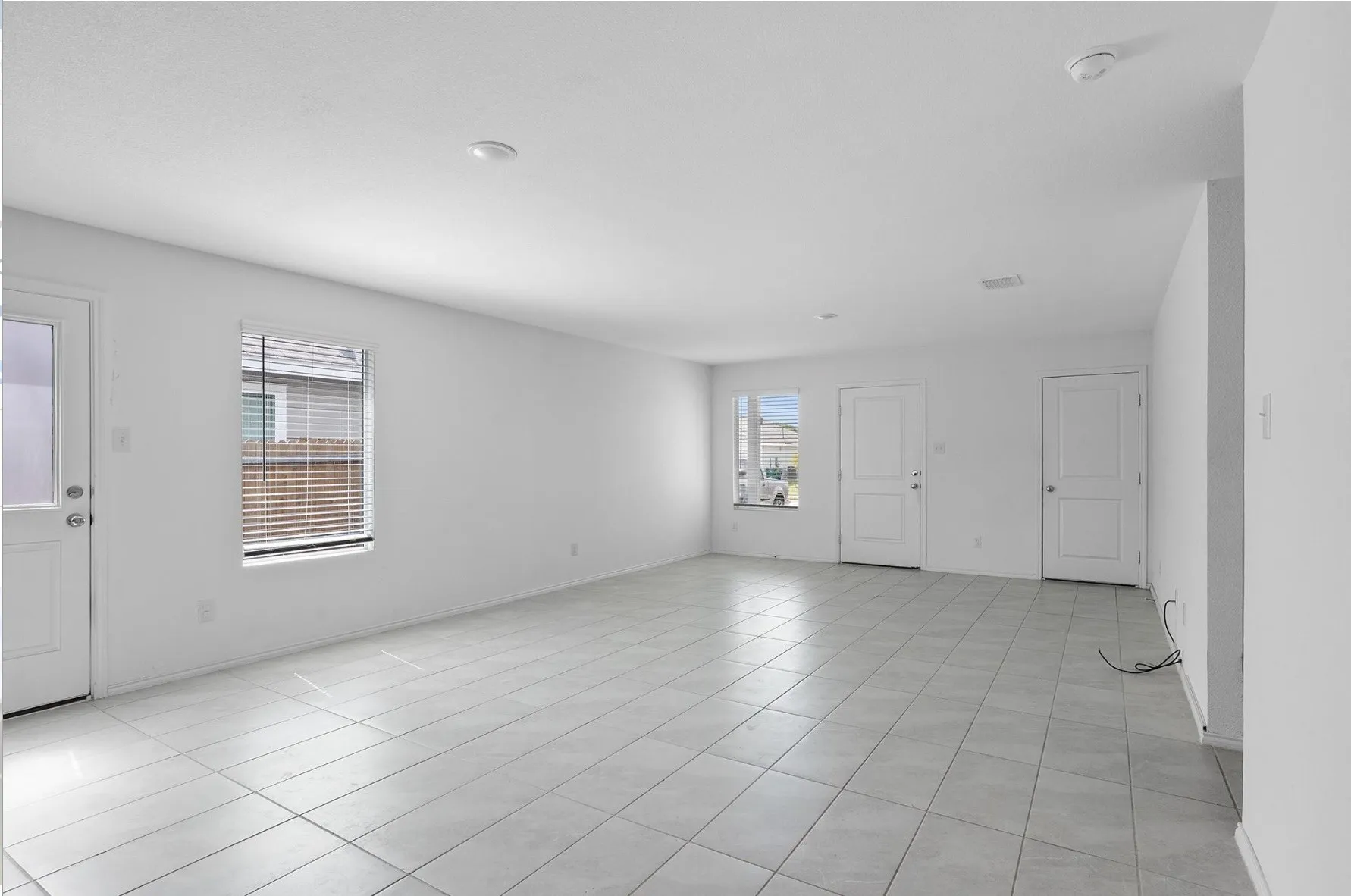 Expansive open-concept room featuring light-toned tile flooring, recessed ceiling lighting, and multiple windows with blinds