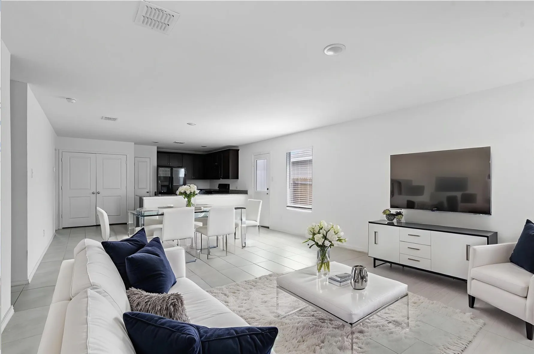 Open-concept living space featuring light-toned tile flooring, recessed lighting, and a kitchen area with dark cabinetry