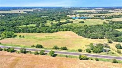 Expansive rural landscape featuring a paved roadway, open fields, wooded areas, and a visible body of water