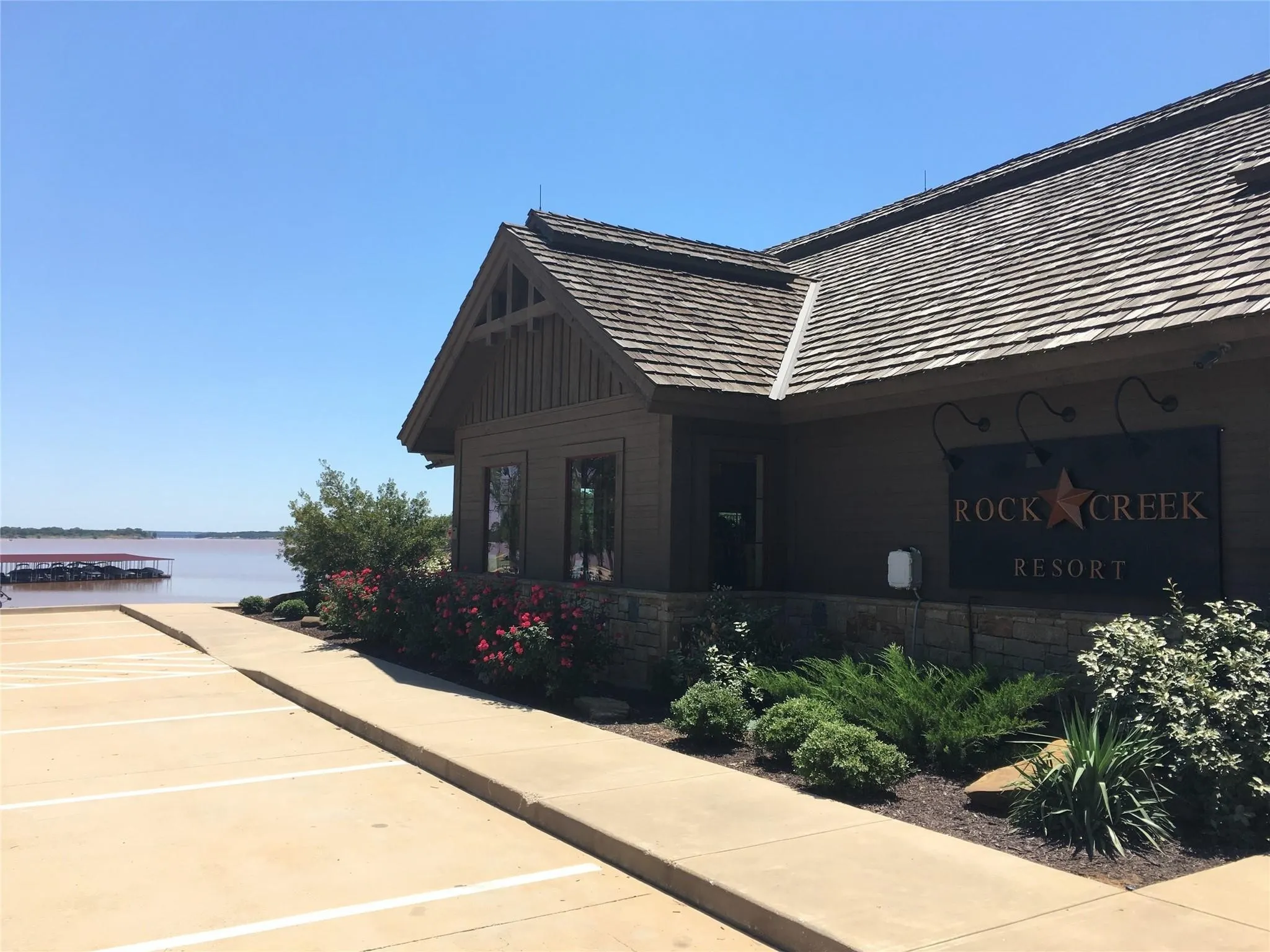 Wood-shingled roof, stone facade, manicured landscaping, concrete walkway, and waterfront access with boat slips