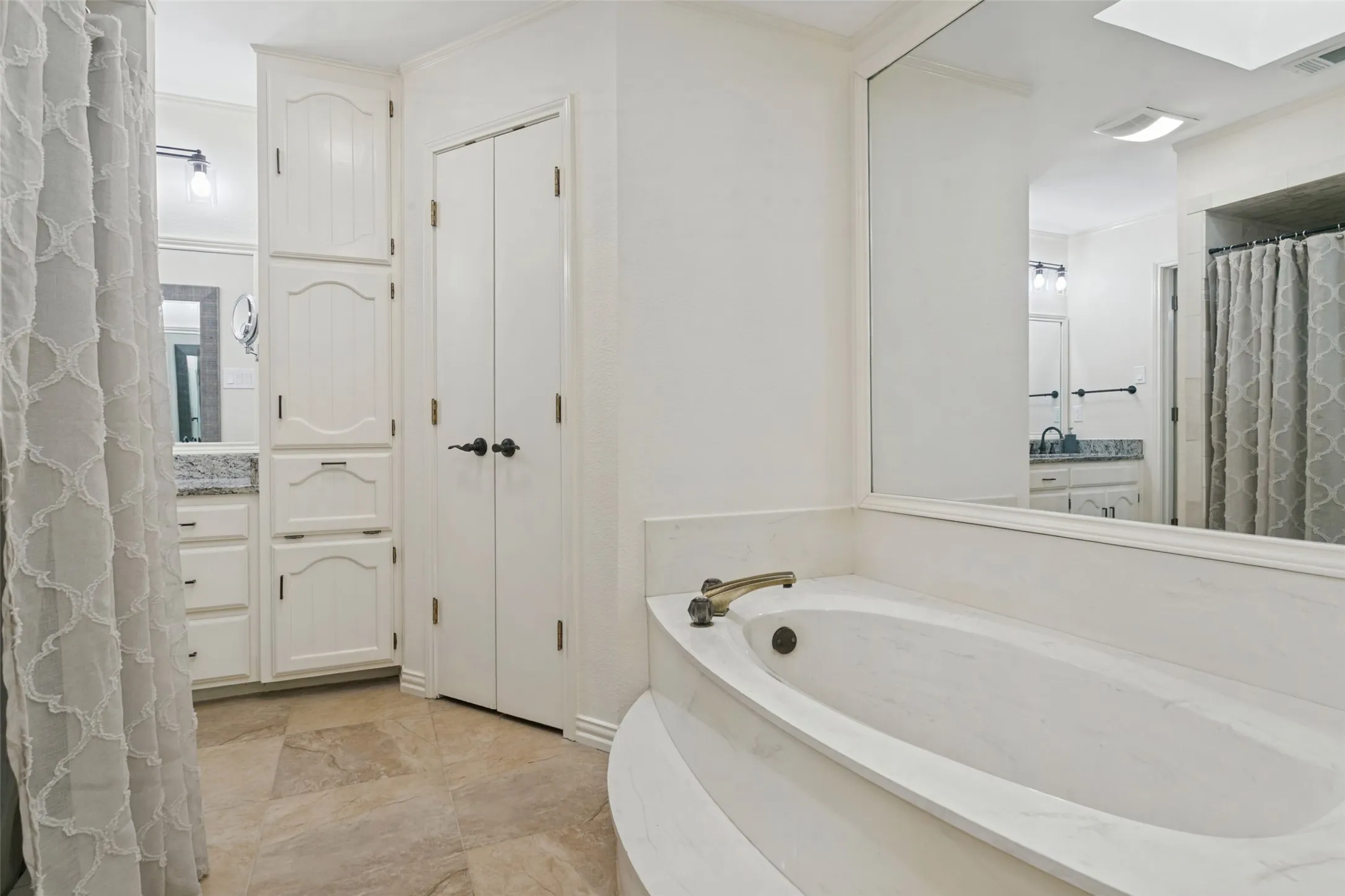 Built-in soaking tub with gold-tone fixtures, tiled flooring, integrated mirror, and white cabinetry