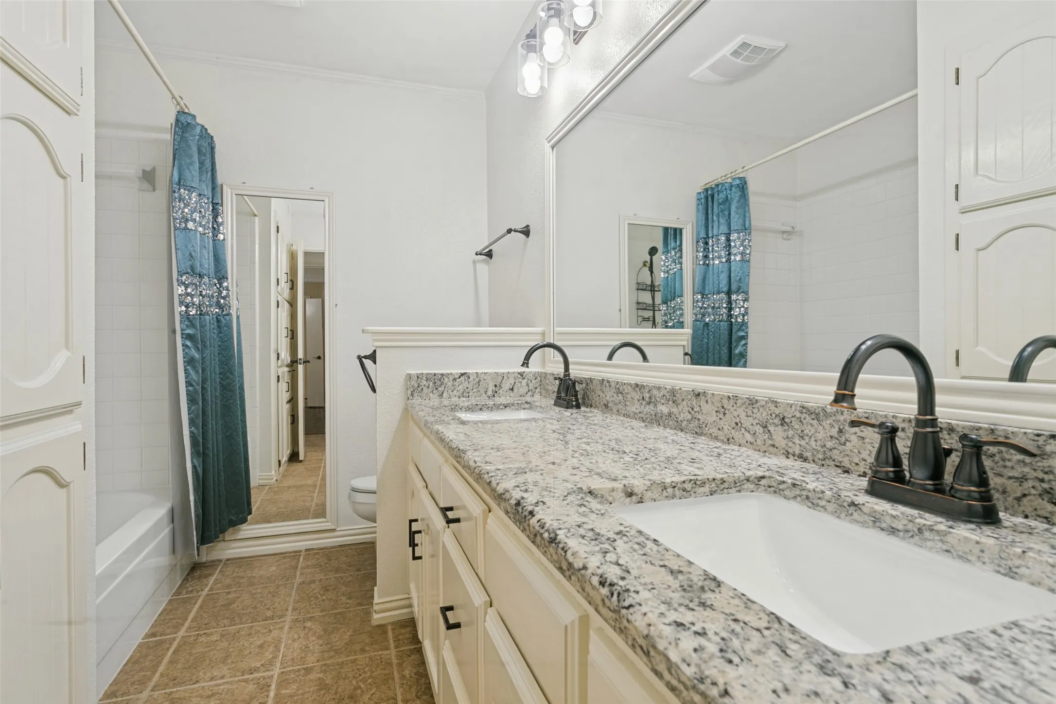 Dual vanity with granite countertops, integrated sinks, dark bronze fixtures, and a large wall-mounted mirror