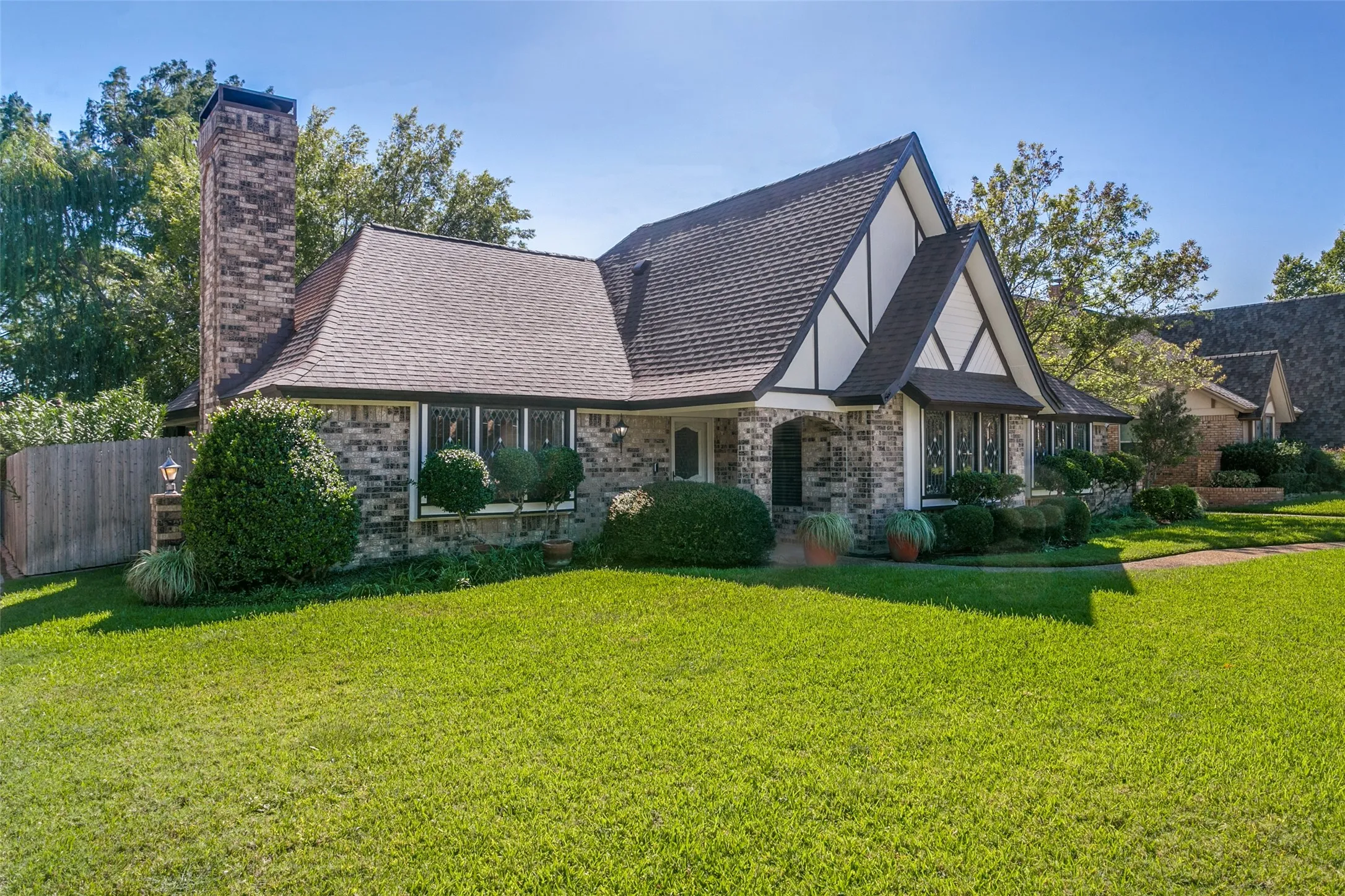 Tudor-style architecture featuring a prominent front gable, brick facade, a large brick chimney, and a well-maintained front lawn