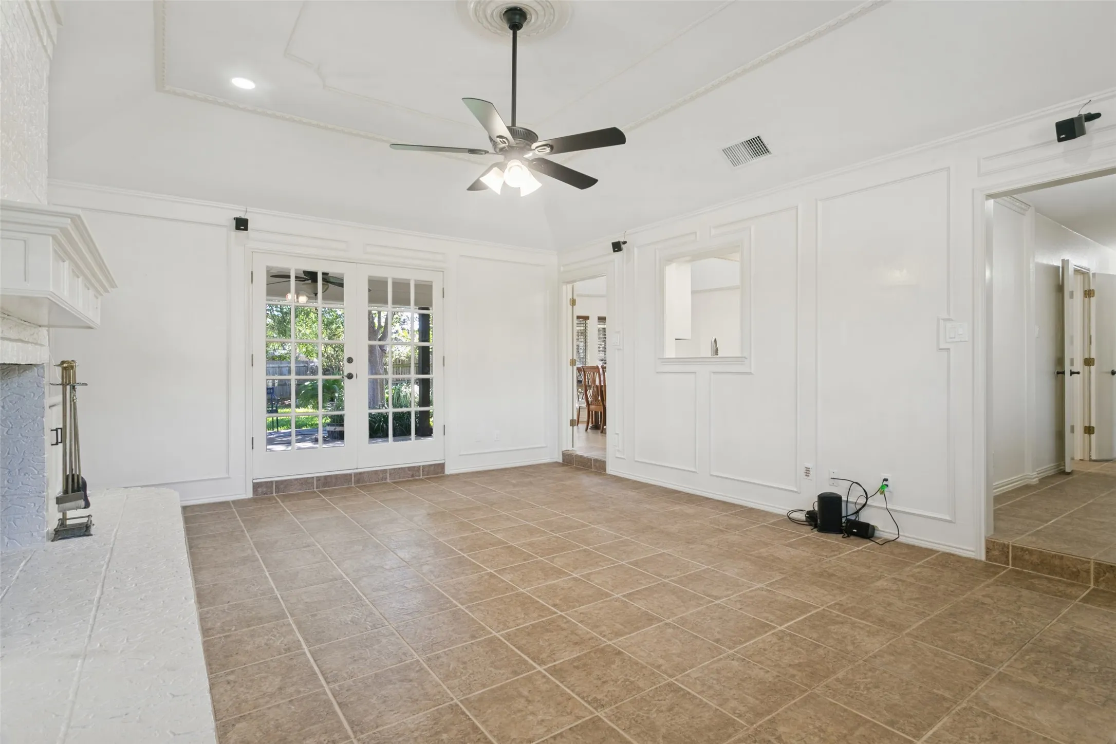 Vaulted ceiling with decorative medallion, ceiling fan, fireplace with mantel, French doors, and tile flooring