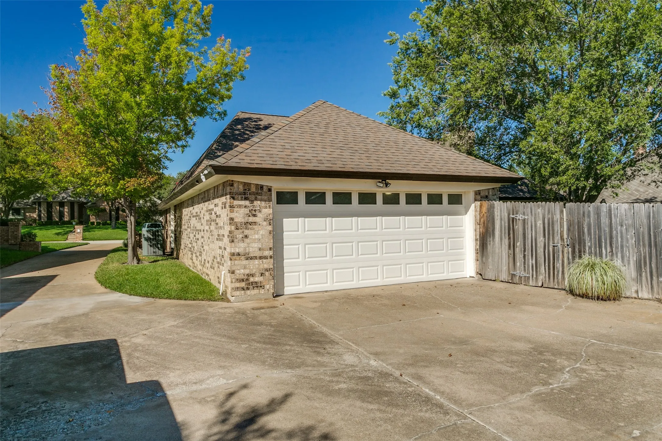 Brick exterior with a brown shingle roof, white panel garage door, and concrete driveway