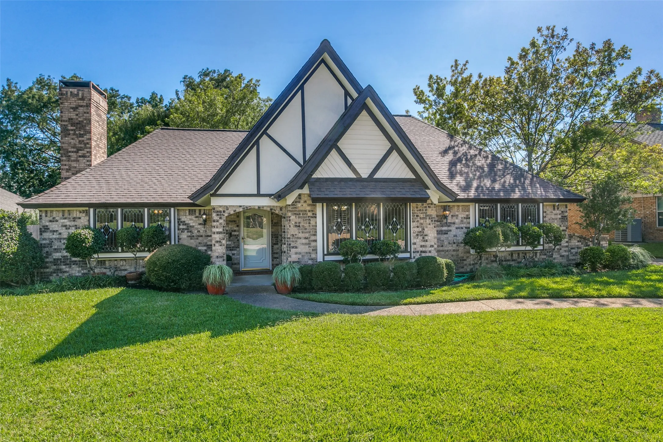 Tudor-style exterior featuring brick and decorative half-timbering, a prominent brick chimney, and a gabled roofline