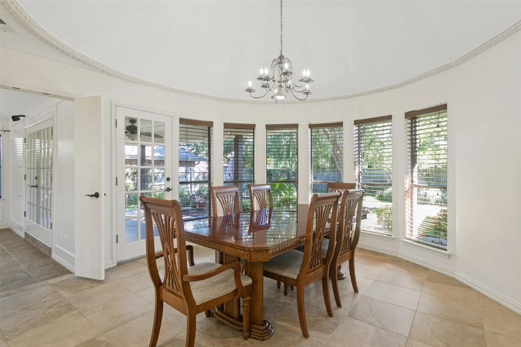 Tray ceiling with decorative molding, chandelier lighting, tiled flooring, multiple windows with blinds, and a French door with glass panels