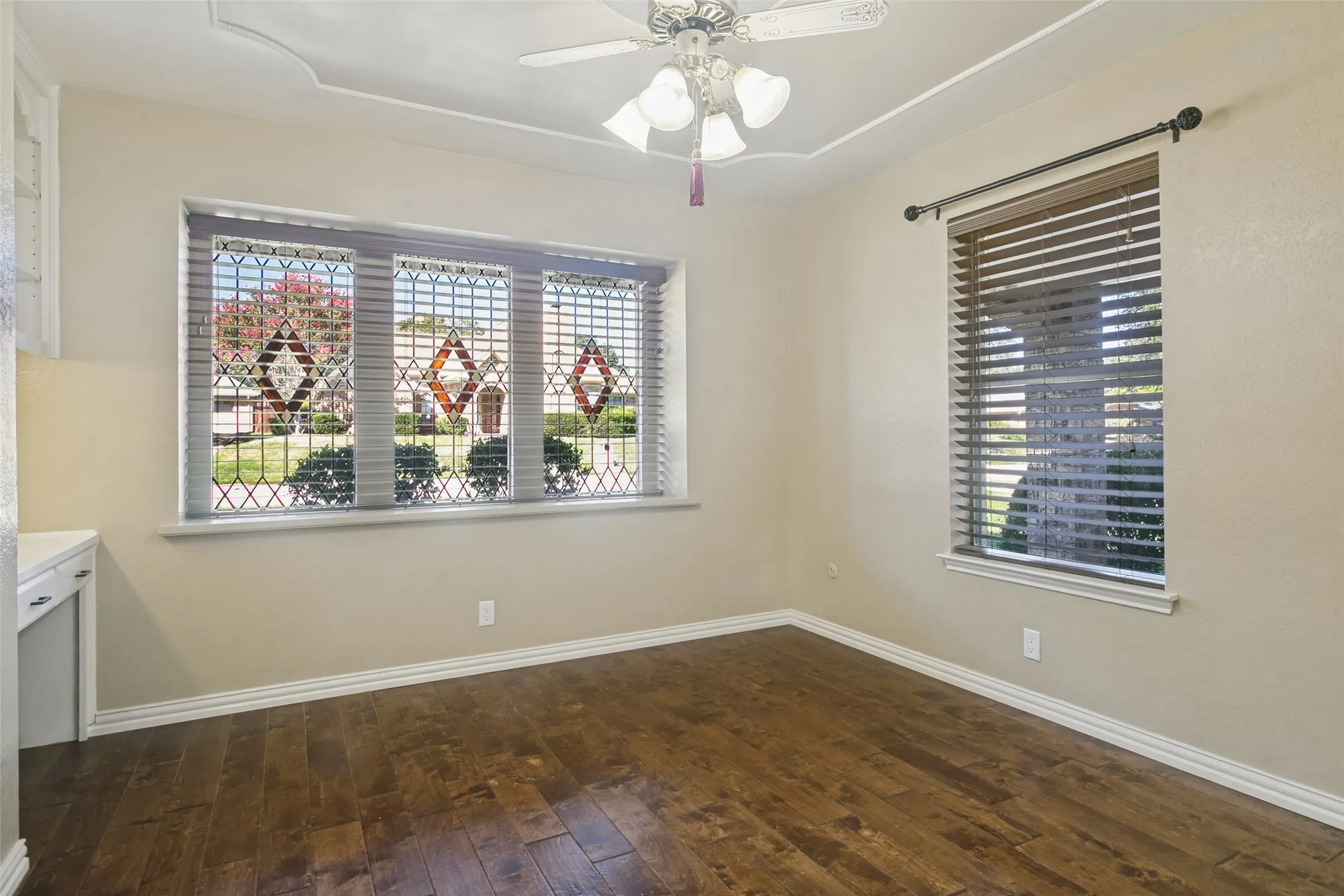 Hardwood-finish flooring, tray ceiling, decorative window security bars, built-in cabinetry, and ceiling fan with light fixture
