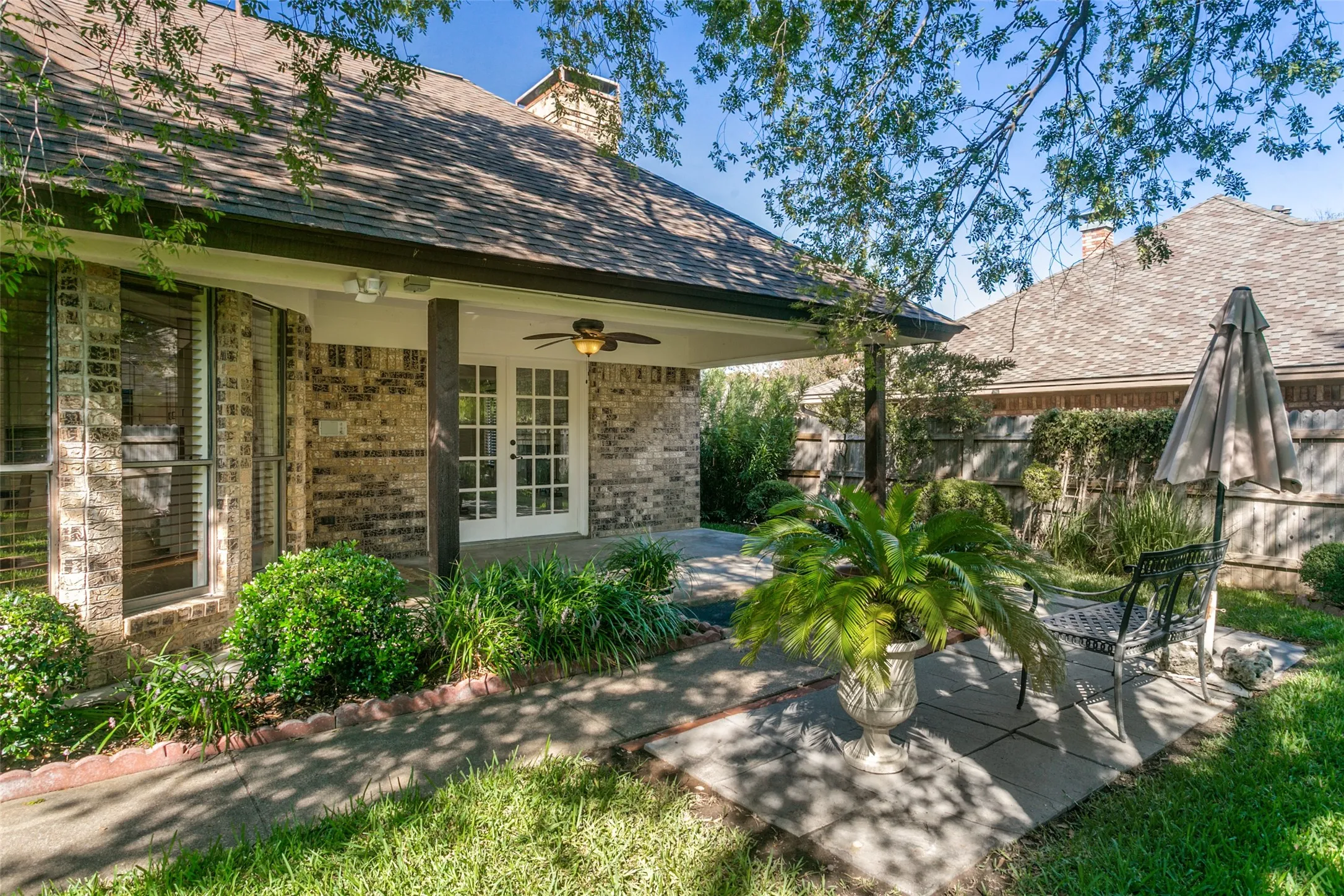 Brick exterior with covered patio, white French doors, and ceiling fan
