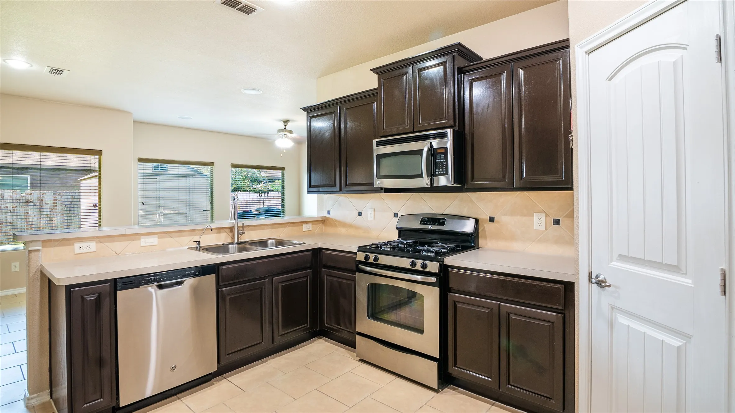 Kitchen featuring dark wood cabinetry, stainless steel appliances, light-toned countertops, tile backsplash, and tile flooring