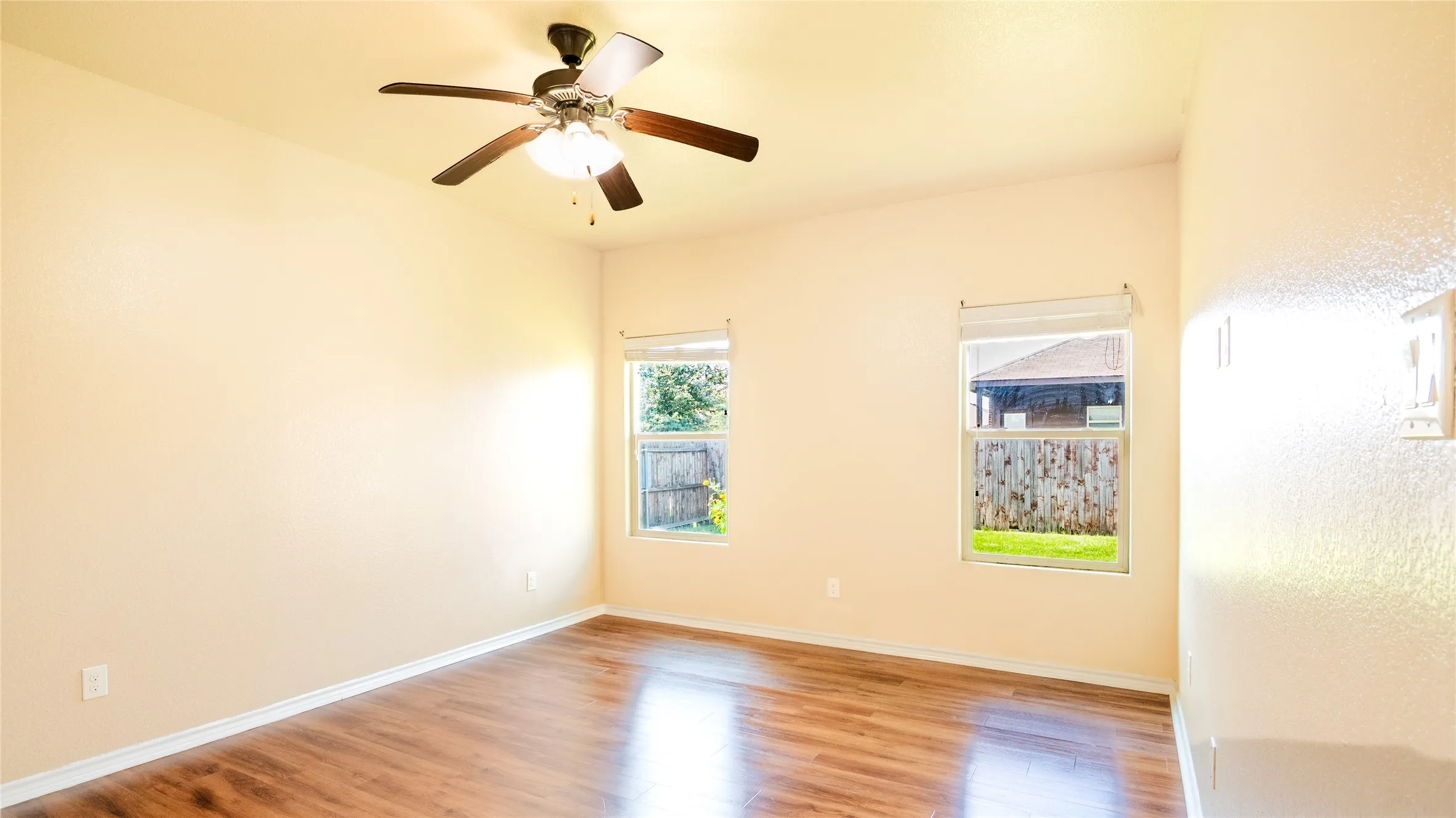 Vaulted ceiling with a ceiling fan, wood-finish flooring, and two windows