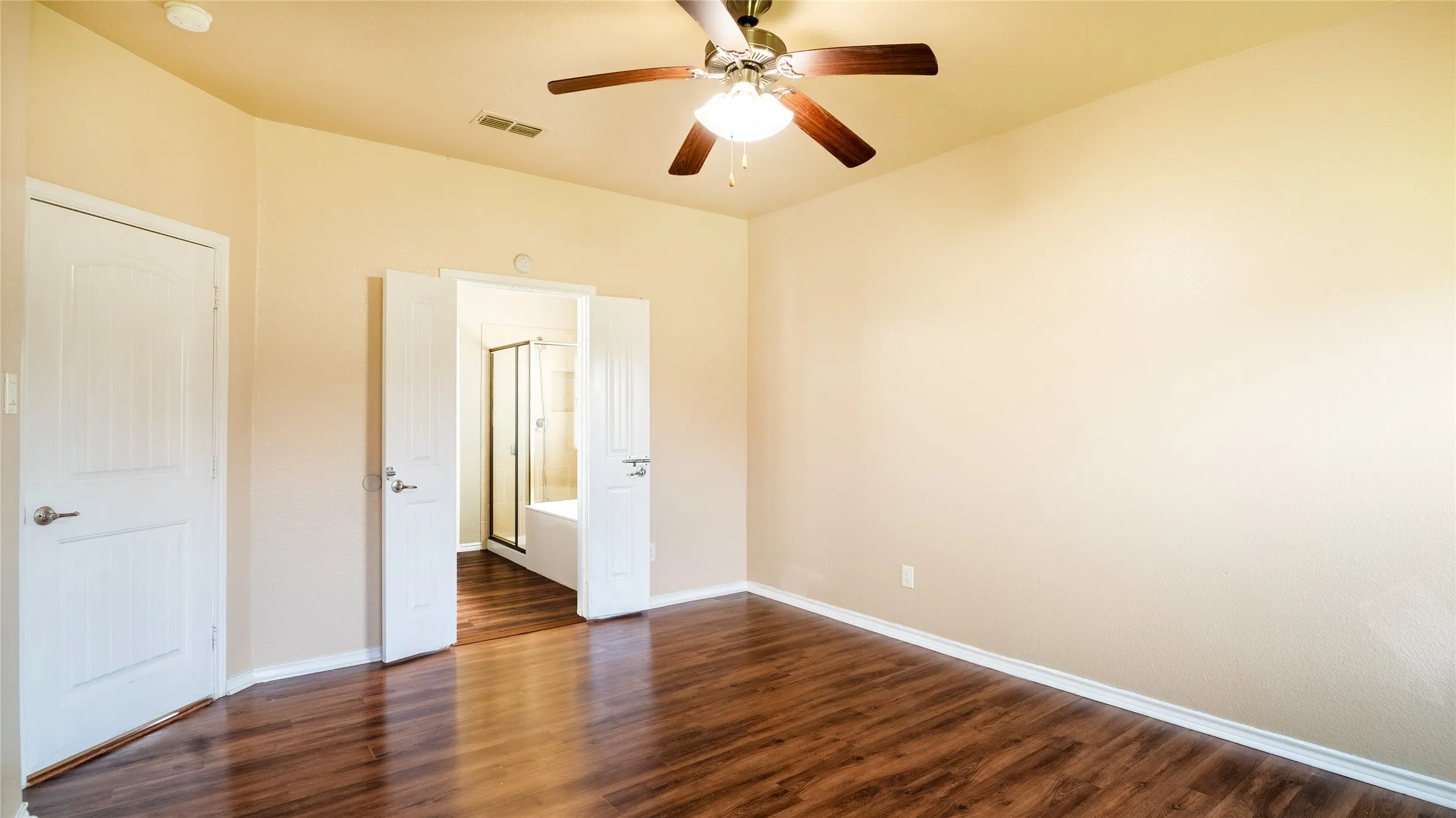 Rich wood-finish flooring, neutral wall tones, and a ceiling fan with integrated lighting