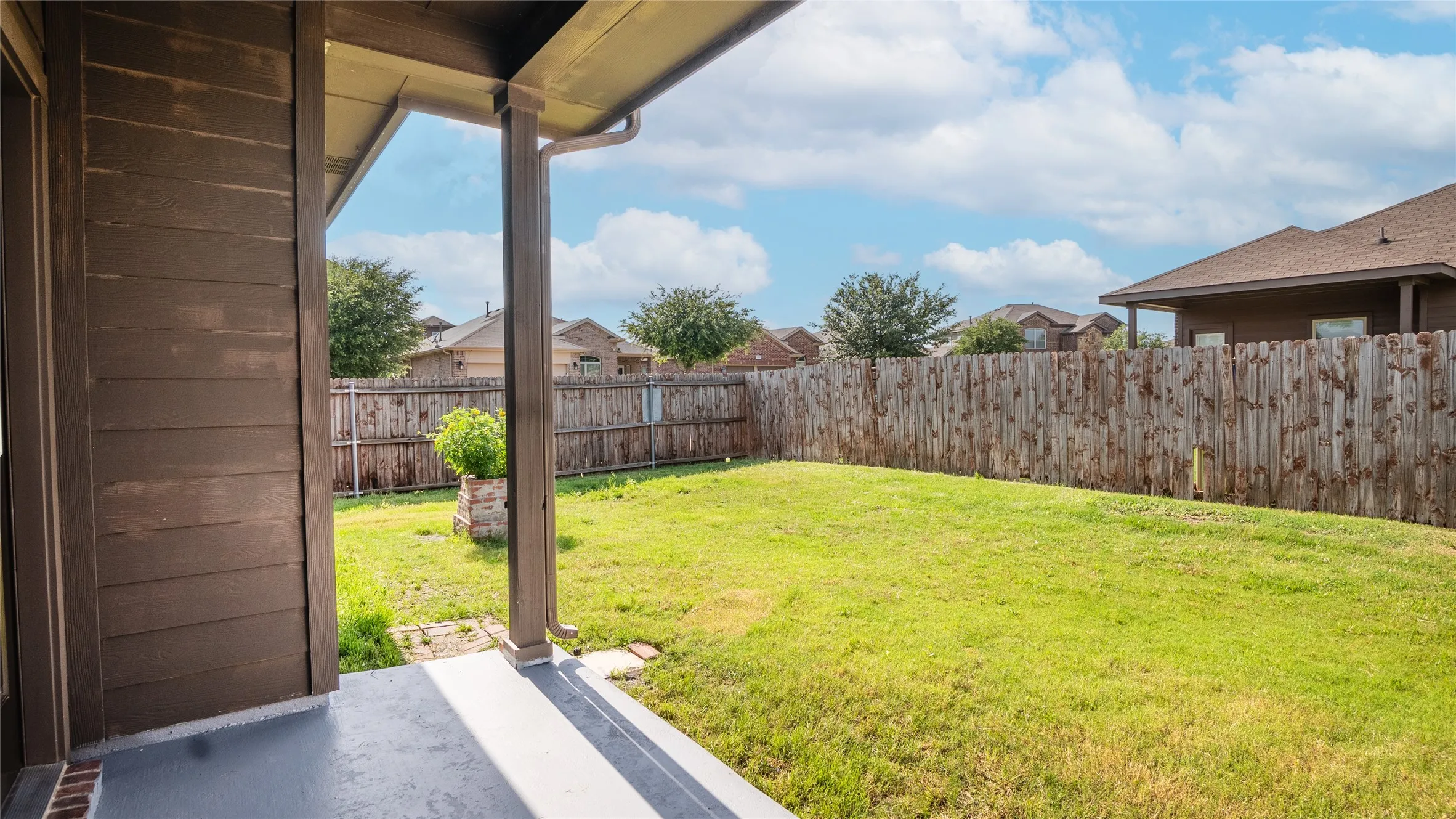 Expansive backyard with a manicured lawn, full wood privacy fencing, and a covered concrete patio