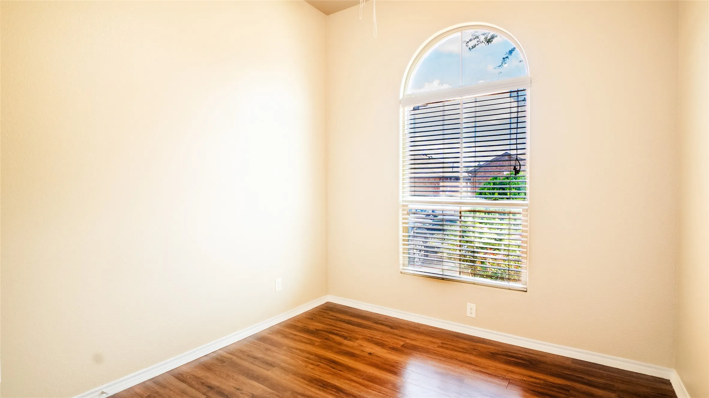 Arch-top window with blinds, wood-finish flooring, and light-toned walls