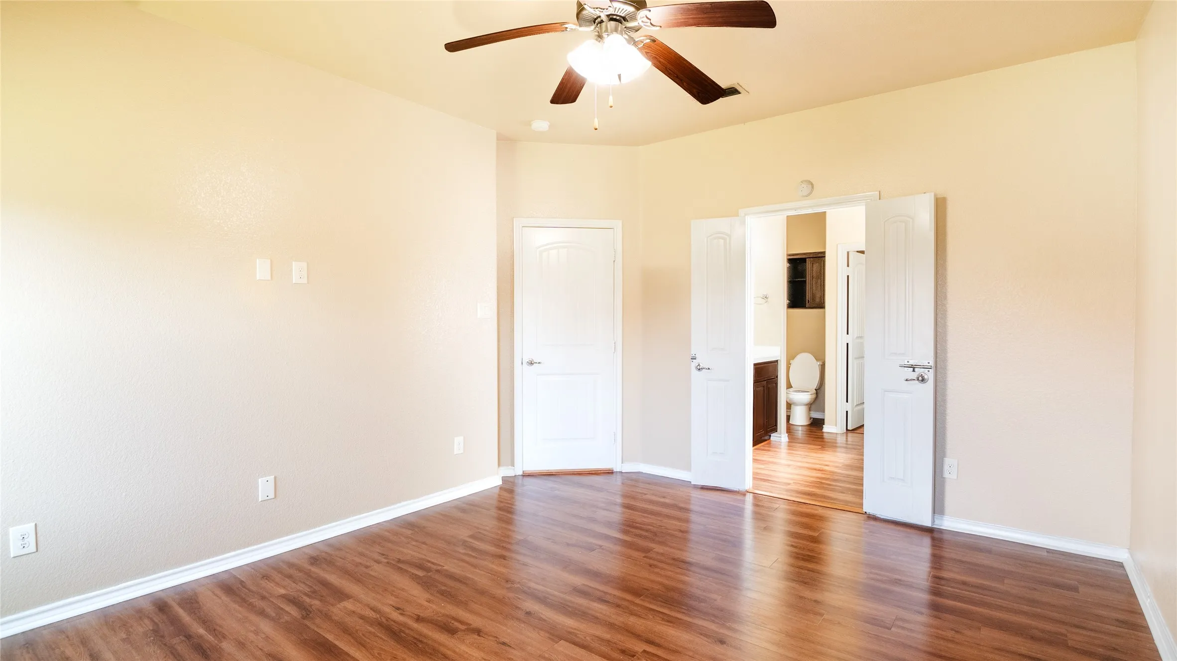 Wood-finish flooring throughout, ceiling fan with integrated lighting, textured walls, and white trim