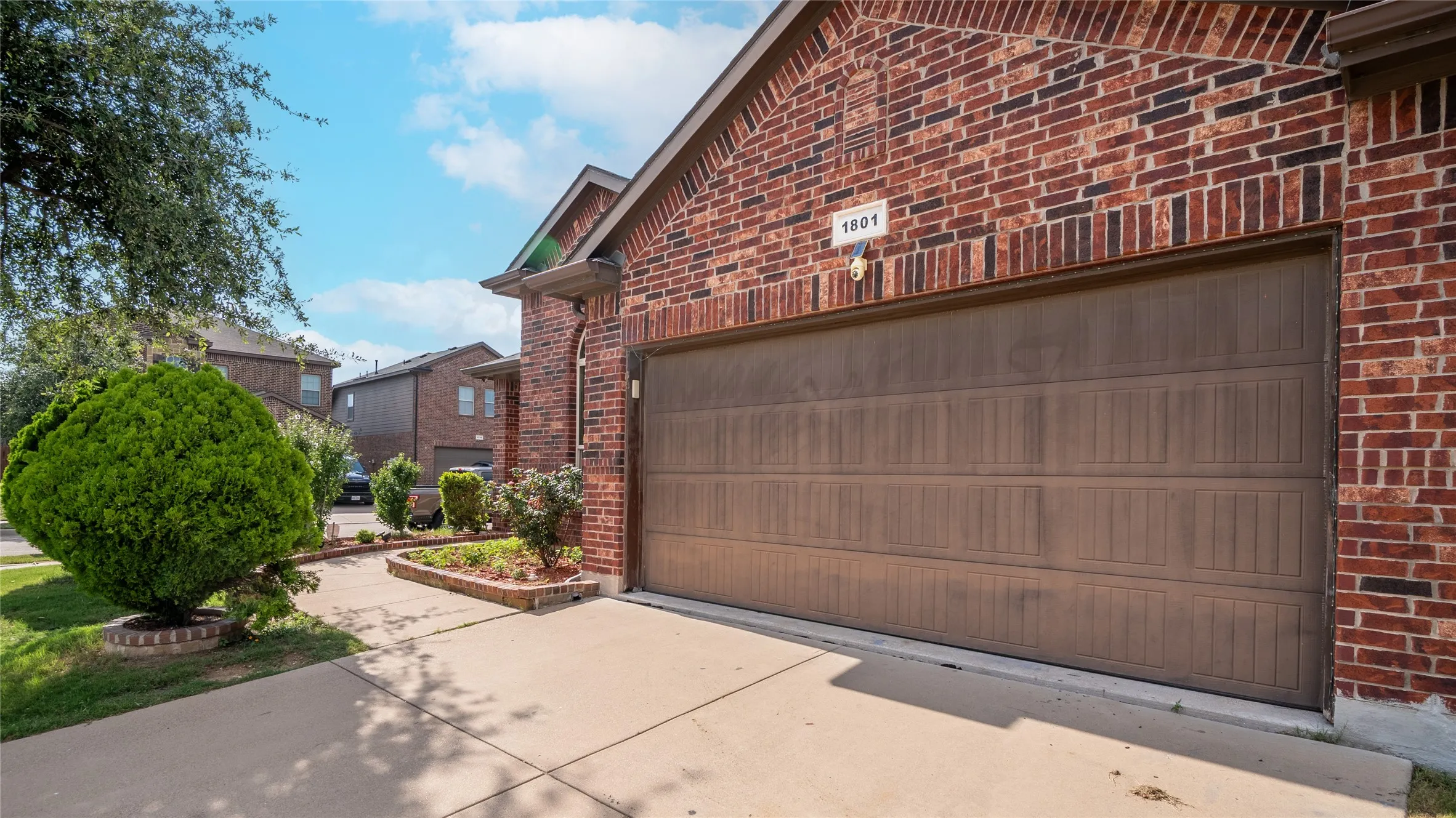 Brick exterior with a brown garage door, concrete driveway, and front landscaping
