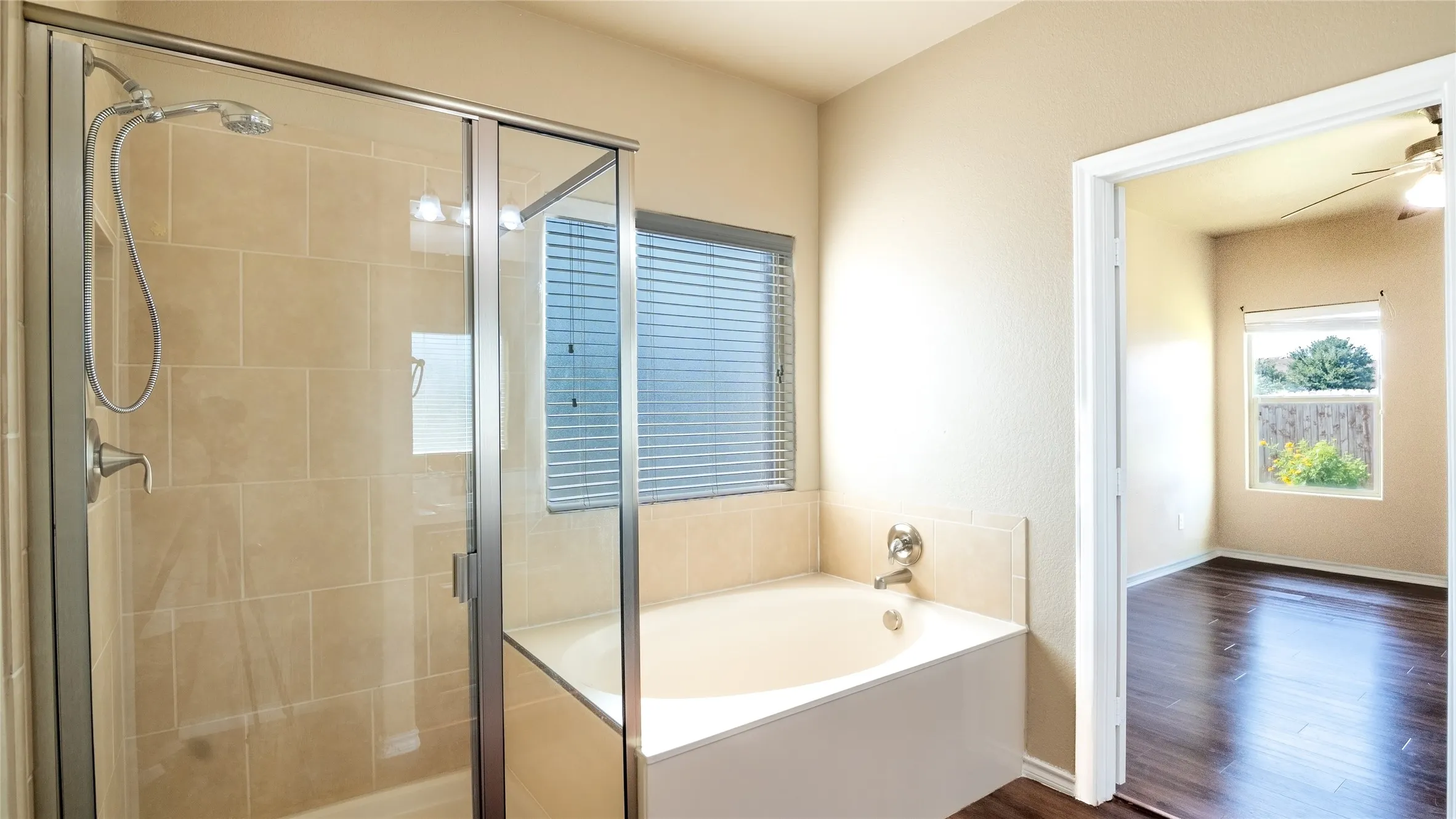 Tiled shower with glass enclosure, separate soaking tub, and window with blinds