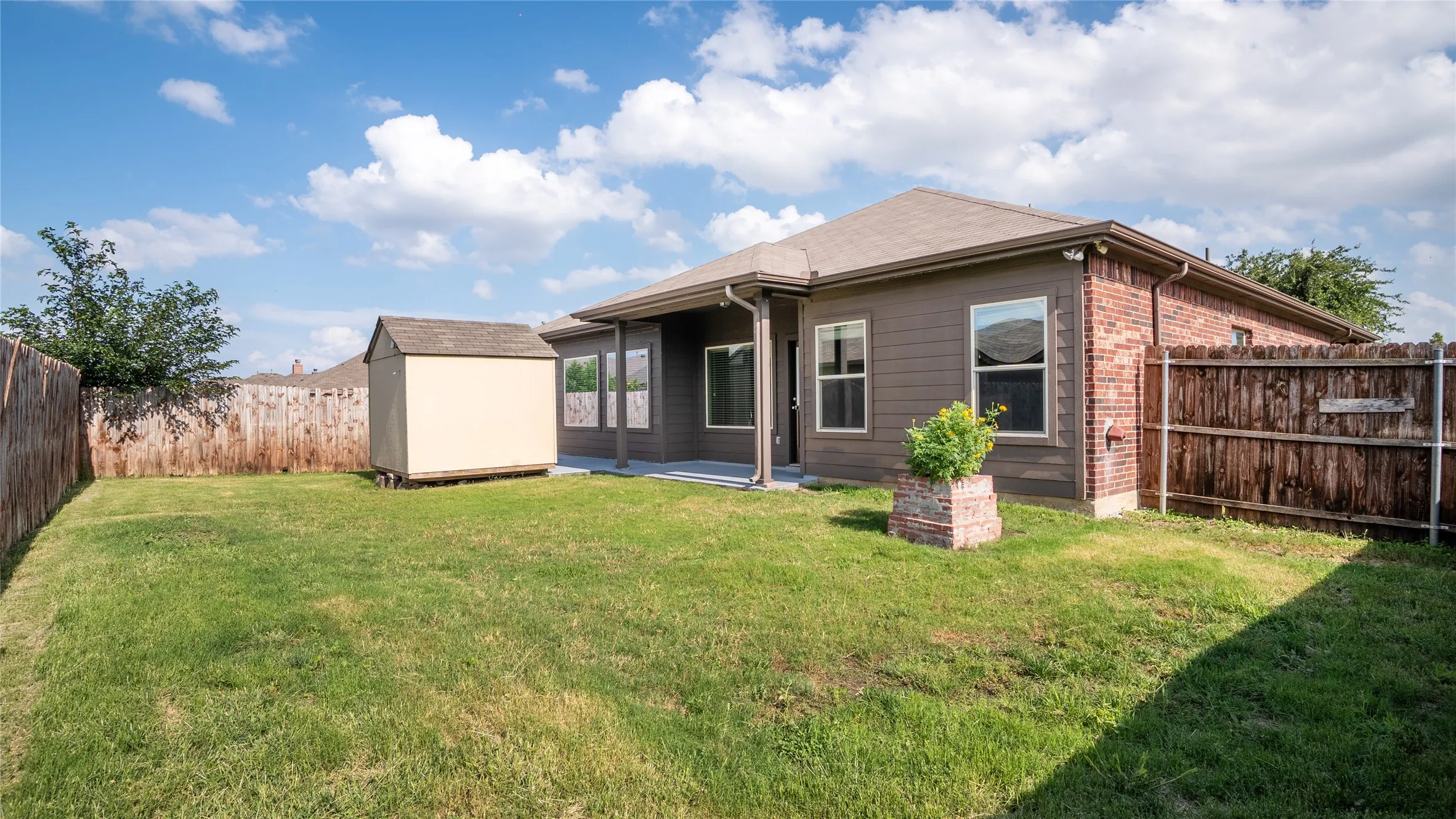 Expansive grass yard with wood fencing, a storage shed, and a covered concrete patio