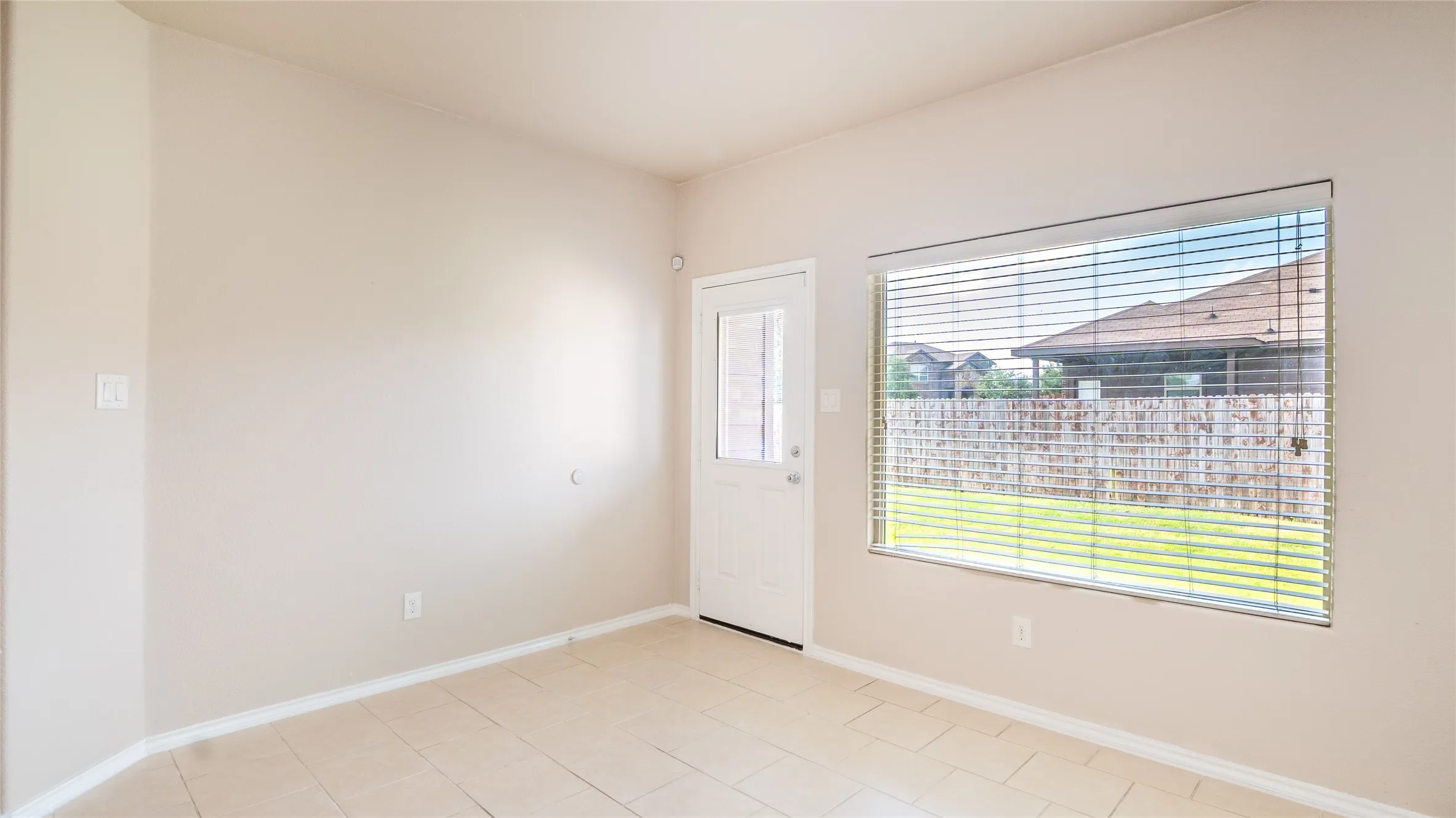 Tile flooring, neutral wall tones, large window with blinds, and a white door with a glass insert