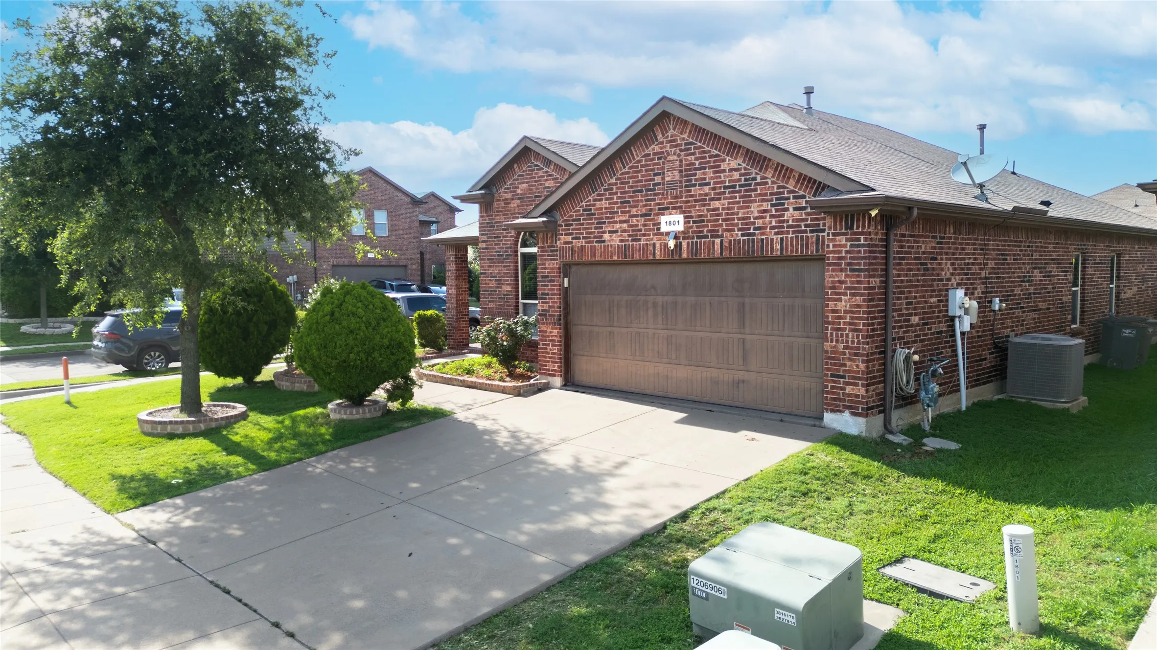 Brick exterior featuring an attached garage with a wood-finish door, concrete driveway, and established front landscaping