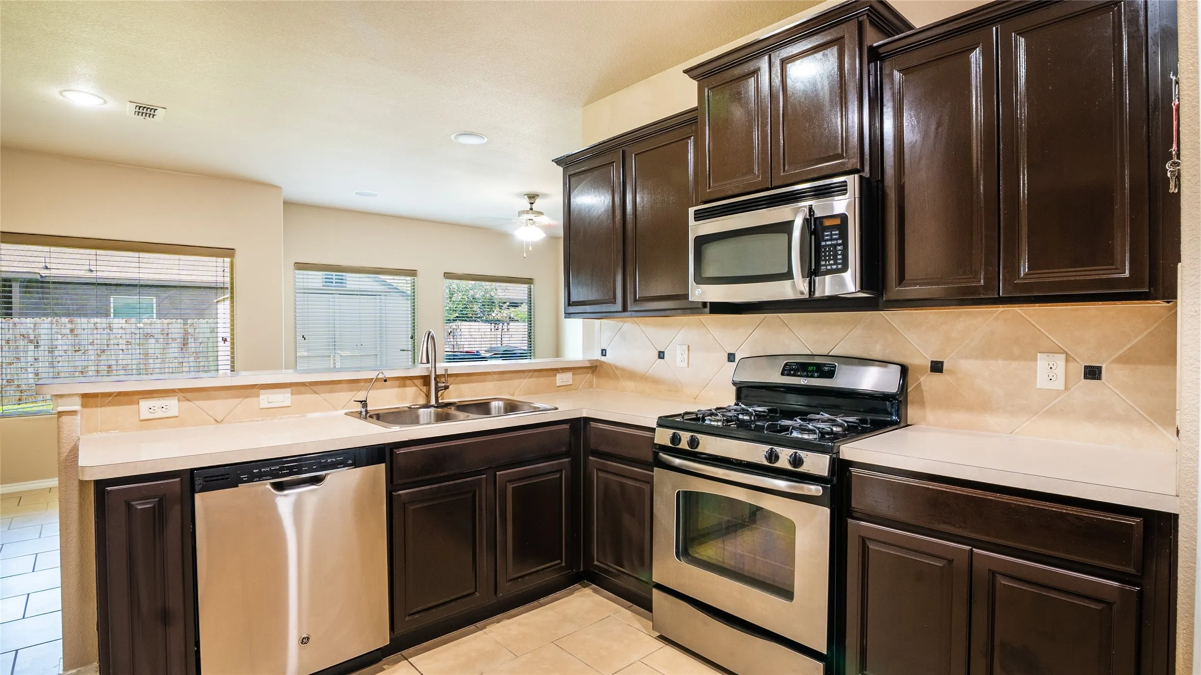 Kitchen featuring dark wood-finish cabinetry, stainless steel appliances, light-toned countertops, and a tiled backsplash